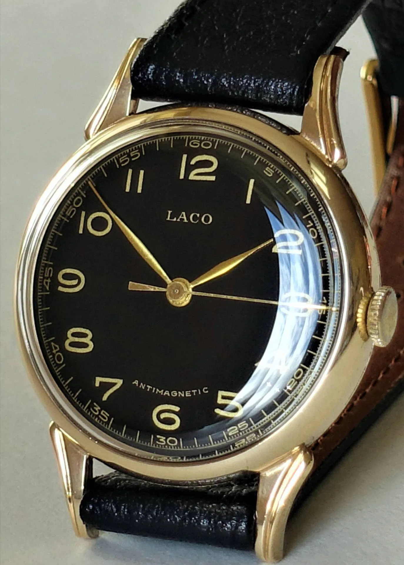 Analoge Armbanduhr mit schwarzem Zifferblatt, goldfarbenem Gehäuse und schwarzem Armband.