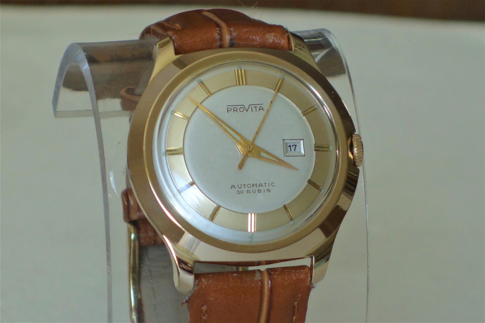 Goldfarbene Armbanduhr mit hellem Zifferblatt, braunem Armband und Datumsanzeige.