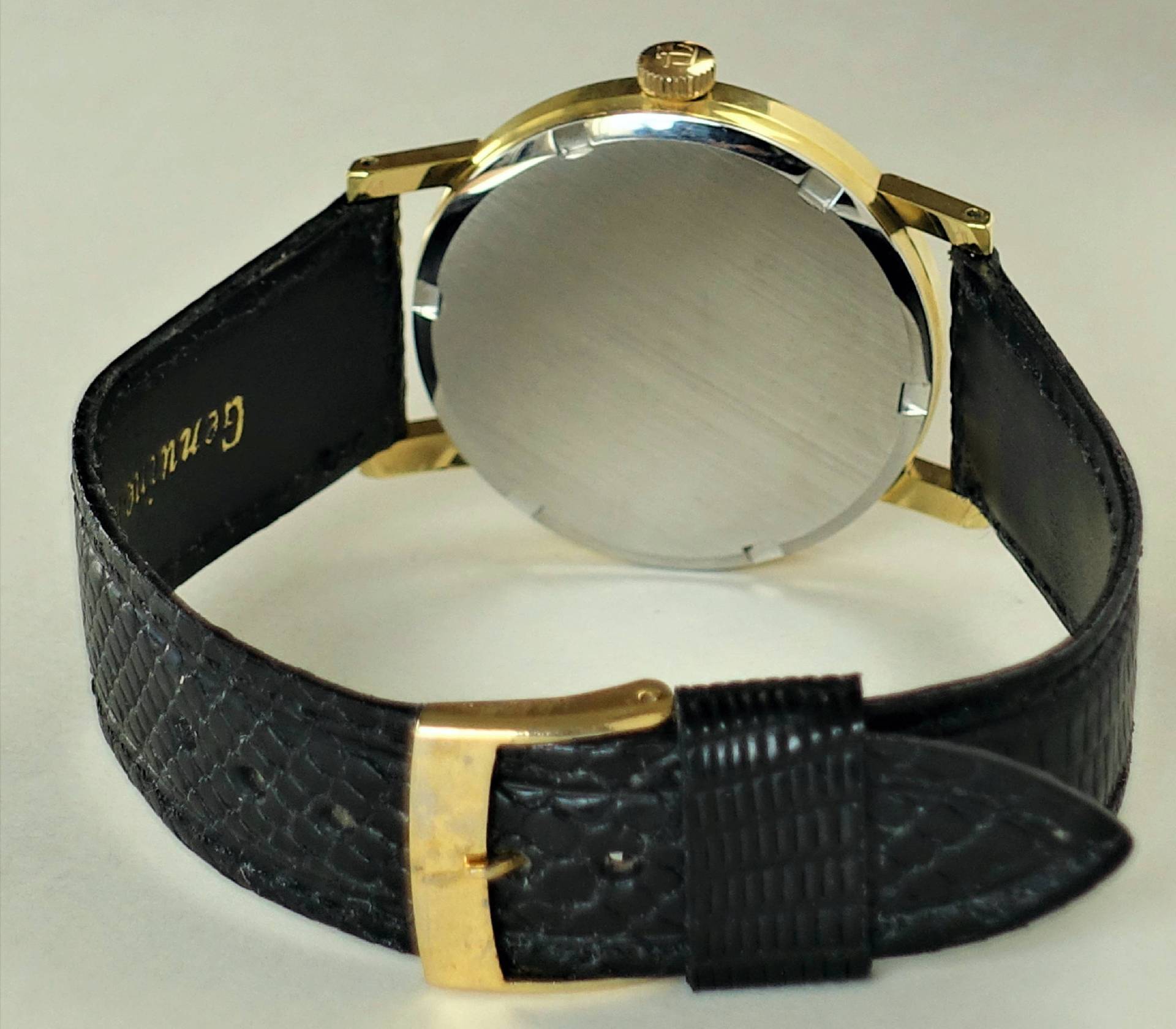 Armbanduhr mit schwarzem Armband und goldfarbenem Gehäuse, Rückseite sichtbar.