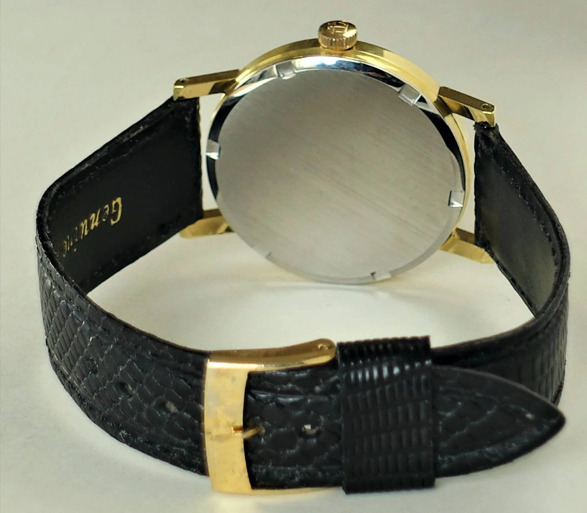 Armbanduhr schwarz goldfarben Armbanduhr mit schwarzem Armband und goldfarbenem Gehäuse, Rückseite sichtbar.