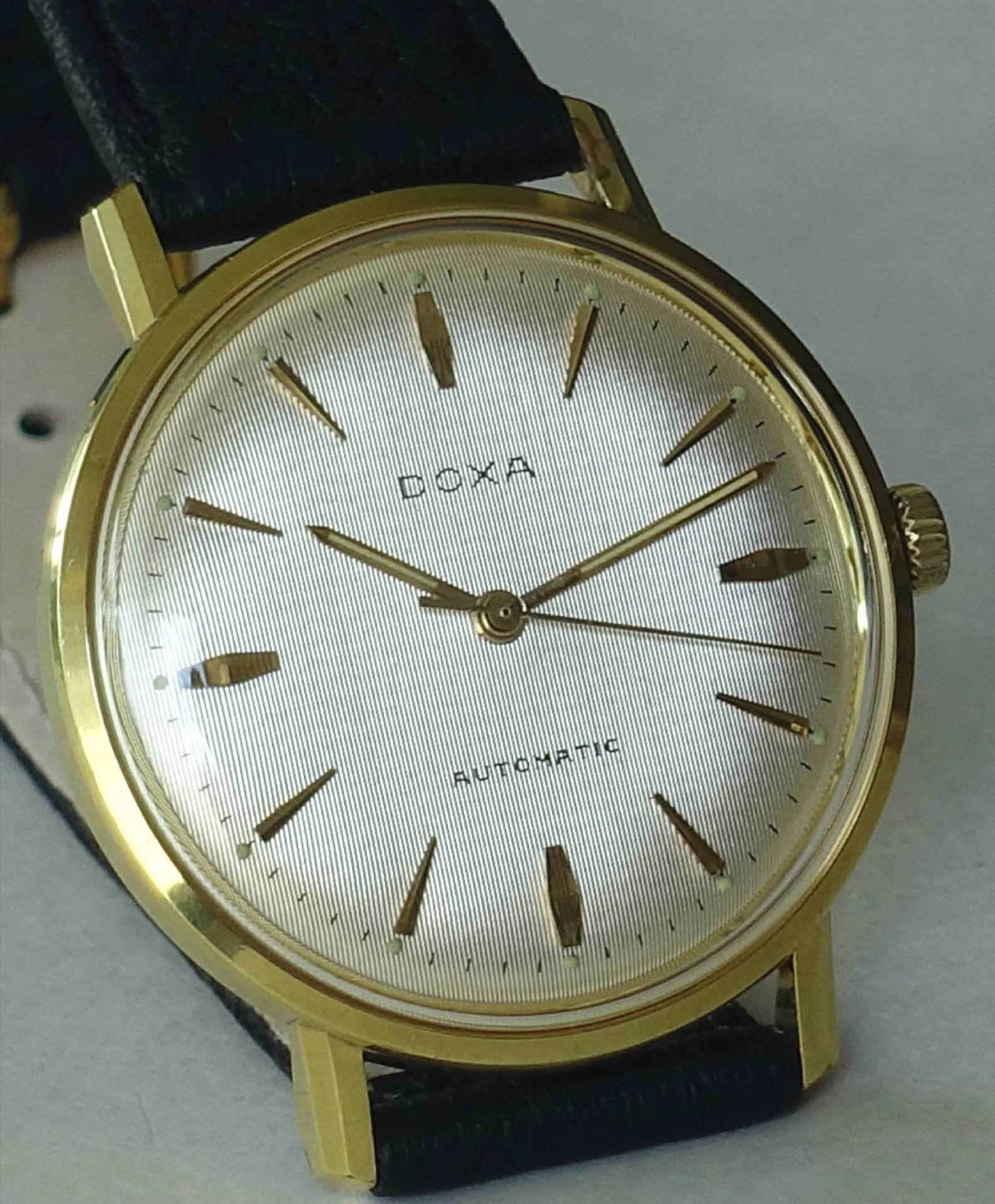 Doxa Armbanduhr goldfarben Goldfarbene Doxa Armbanduhr mit hellem Zifferblatt und schwarzem Armband.
