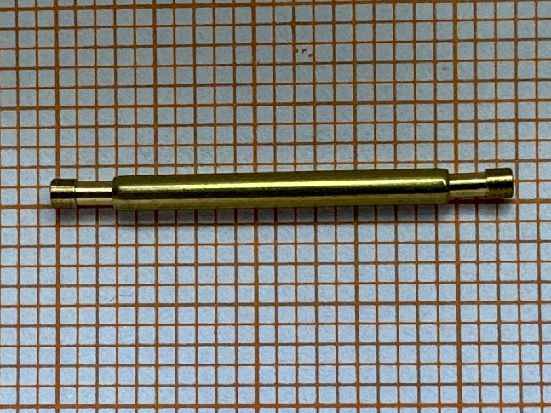 Metallene Aufzugswelle für Armbanduhren auf kariertem Hintergrund.