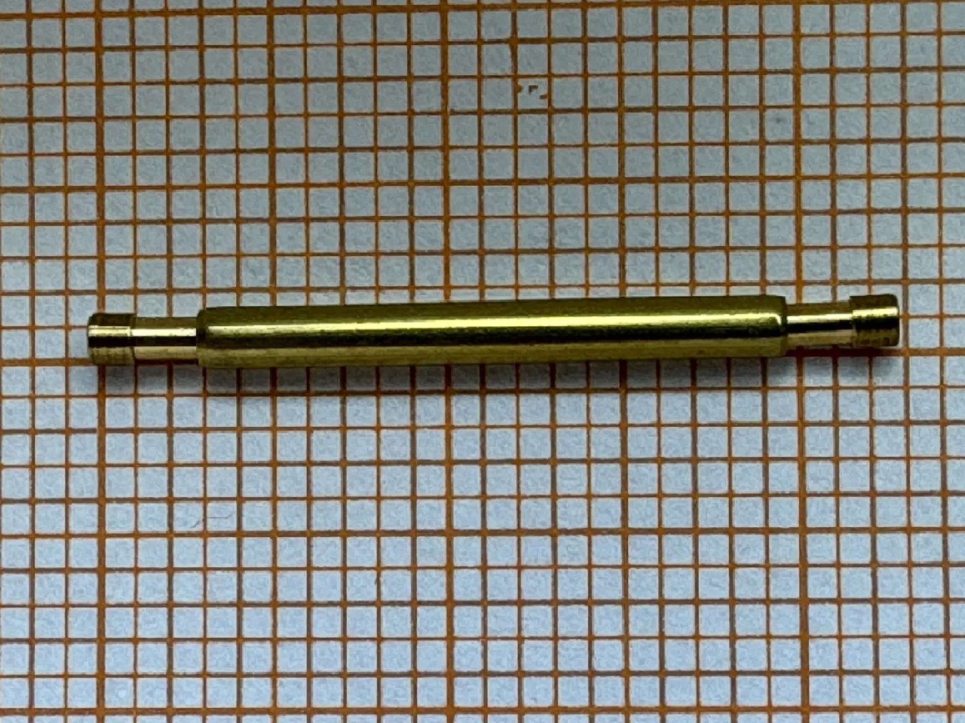 Metallene Aufzugswelle für Armbanduhren auf kariertem Hintergrund.