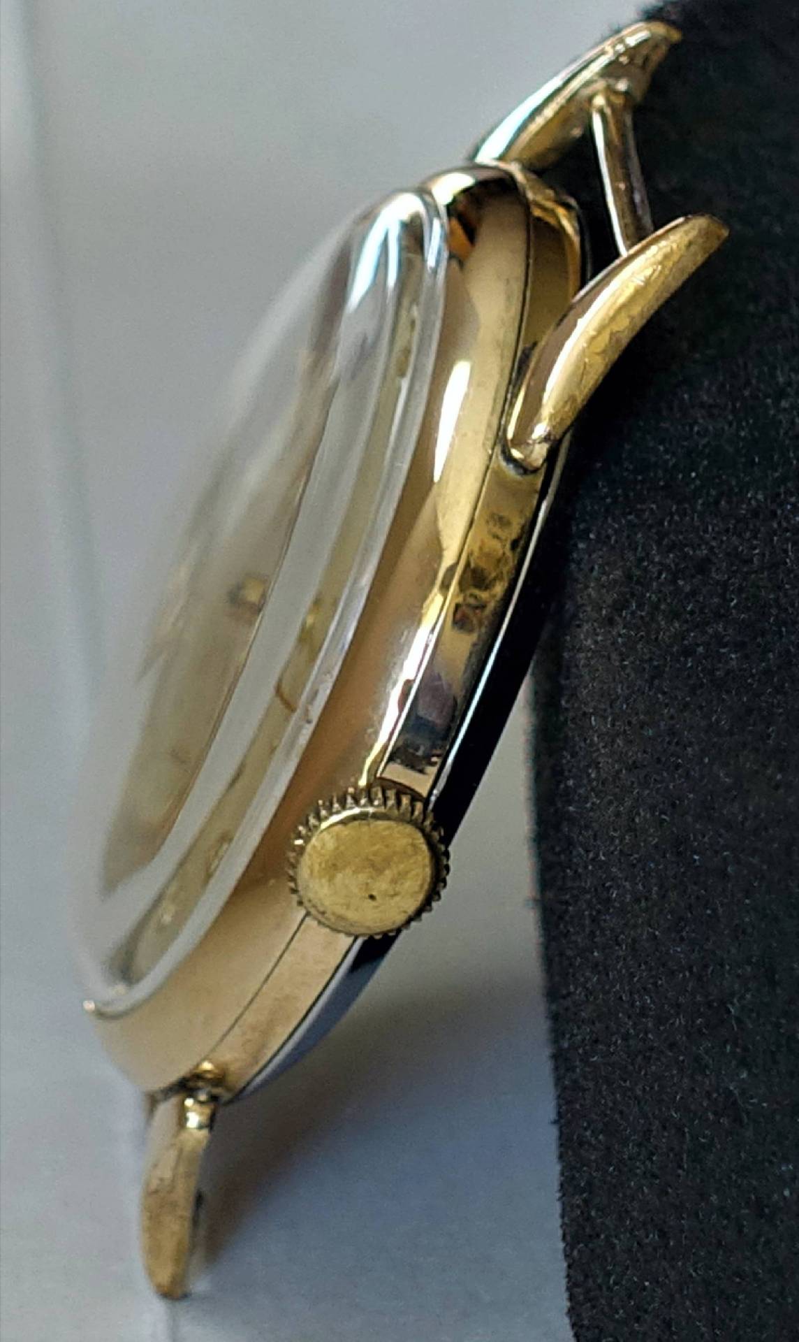 Seitliche Ansicht eines goldfarbenen Uhrgehäuses mit Krone und aufgesetztem Uhrglas.