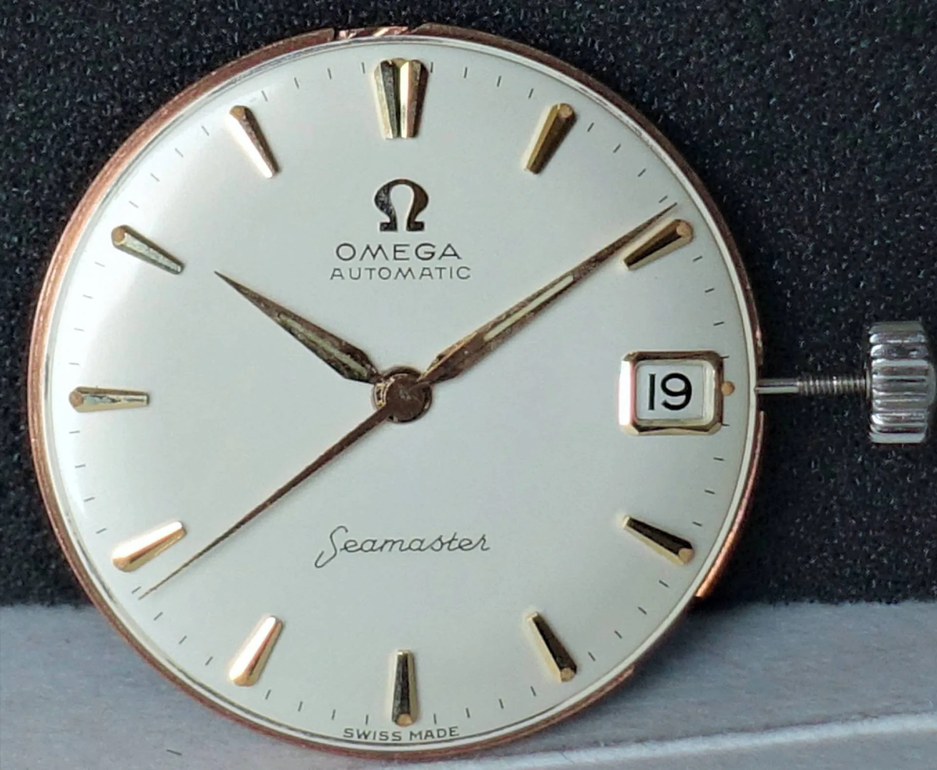 Omega Seamaster Uhrwerk Rundes Uhrwerk mit weißem Zifferblatt, goldfarbenen Indizes und Zeigern, Datumsanzeige und seitlicher silberfarbener Krone.