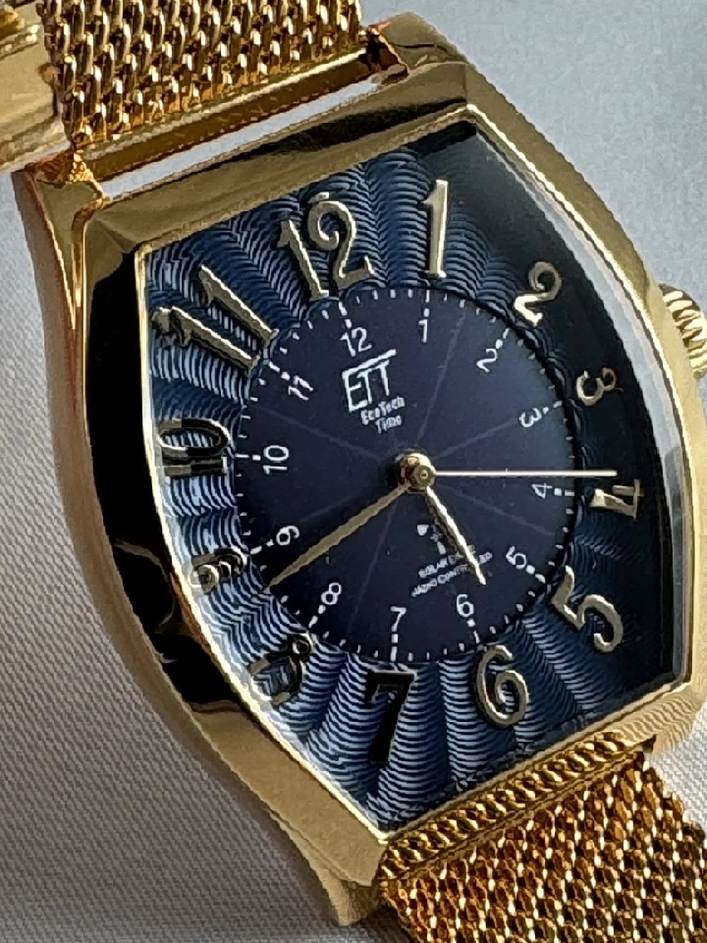 Goldfarbene Armbanduhr mit blauem Zifferblatt, arabischen Zahlen und goldfarbenem Mesharmband.