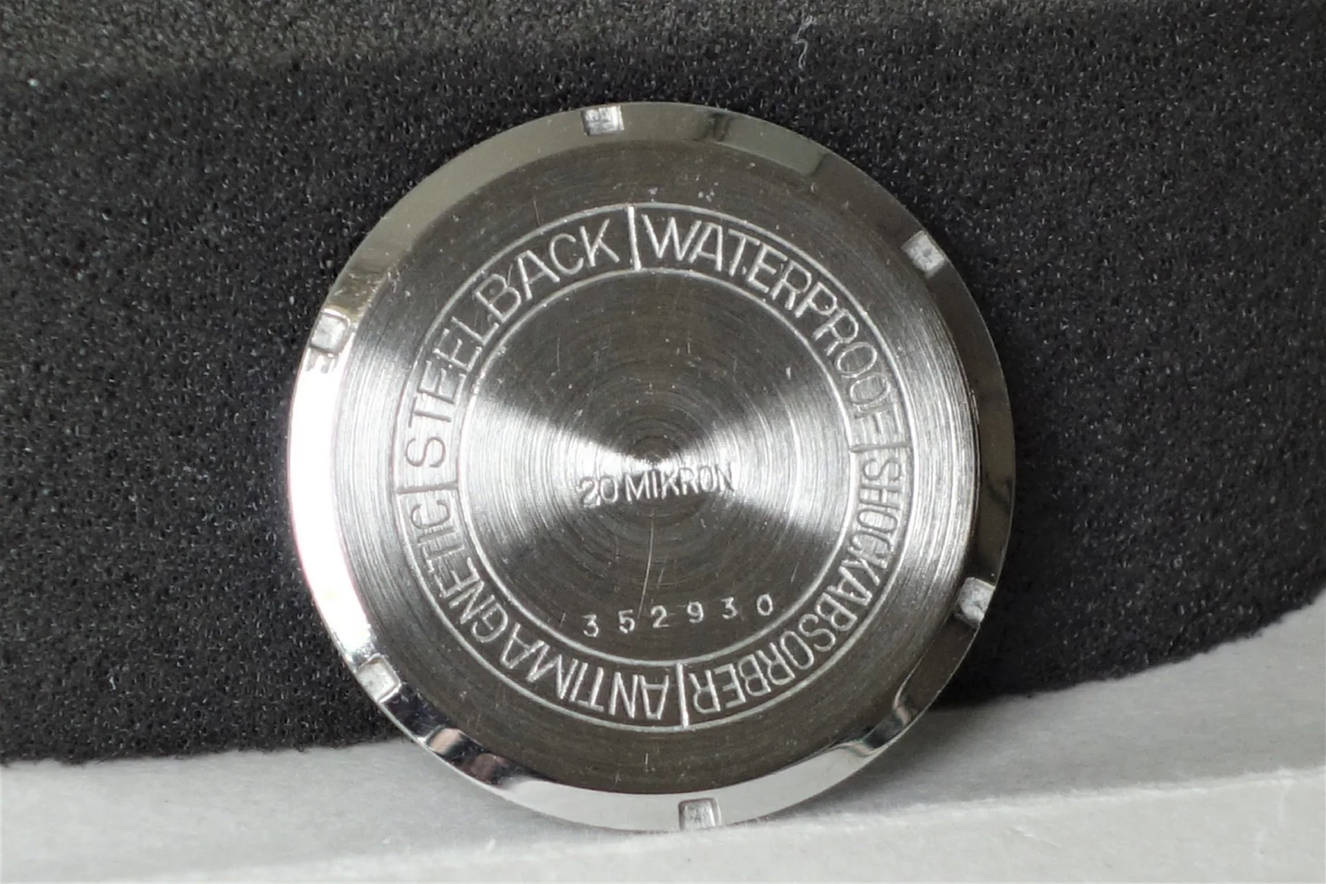 Runder silberfarbener Uhrenboden mit Gravur und polierter Oberfläche.