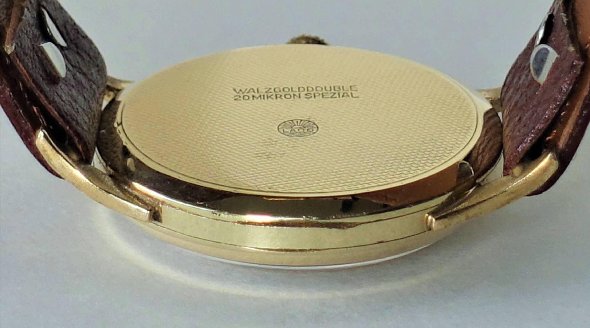 Goldfarbener Uhrenboden mit feiner Struktur und Gravur, befestigt an einem braunen Armband.