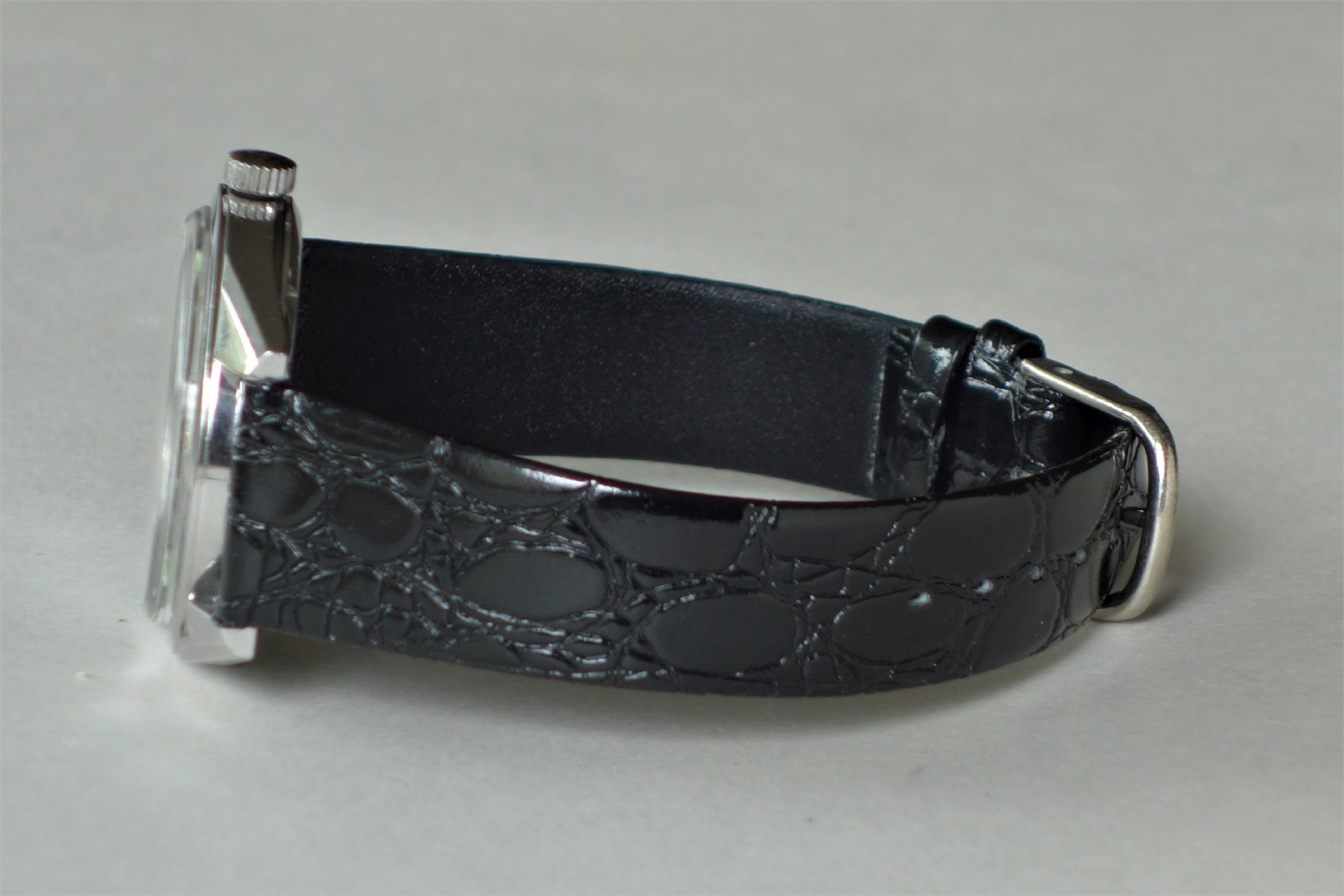 Schwarzes Uhrenarmband mit Prägung und silberfarbener Schließe an einem Uhrgehäuse.