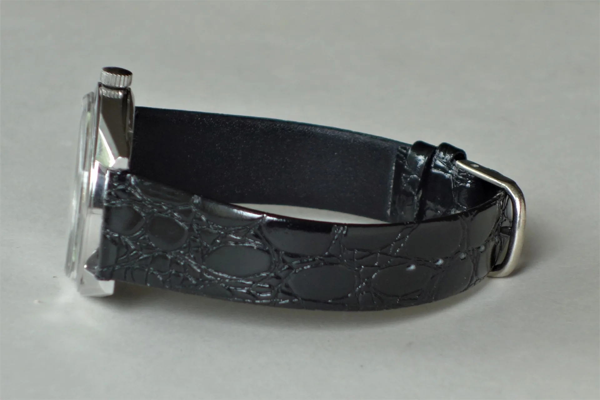 Schwarzes Uhrenarmband mit Prägung und silberfarbener Schließe an einem Uhrgehäuse.