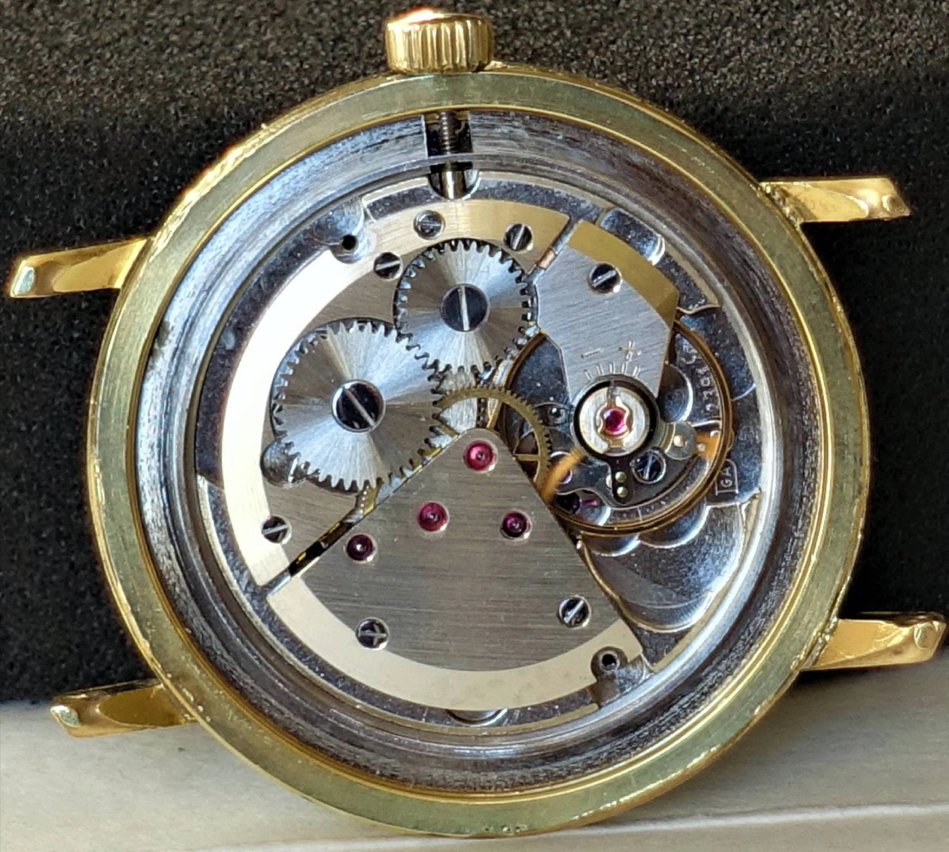Mechanisches Uhrwerk im Gehäuse Mechanisches Uhrwerk in einem goldfarbenen Uhrengehäuse mit sichtbaren Zahnrädern und Rubinlagern.