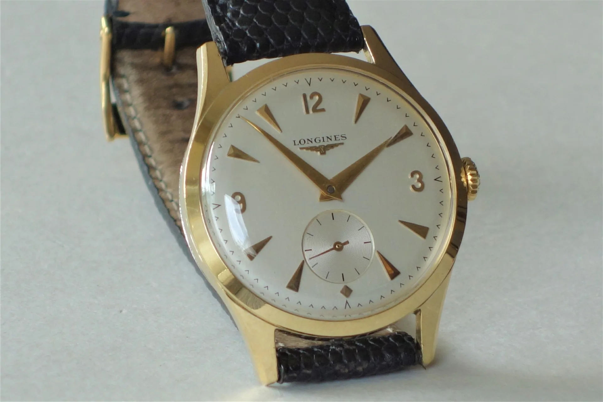 Goldfarbene Armbanduhr mit weißem Zifferblatt und schwarzem Lederarmband.