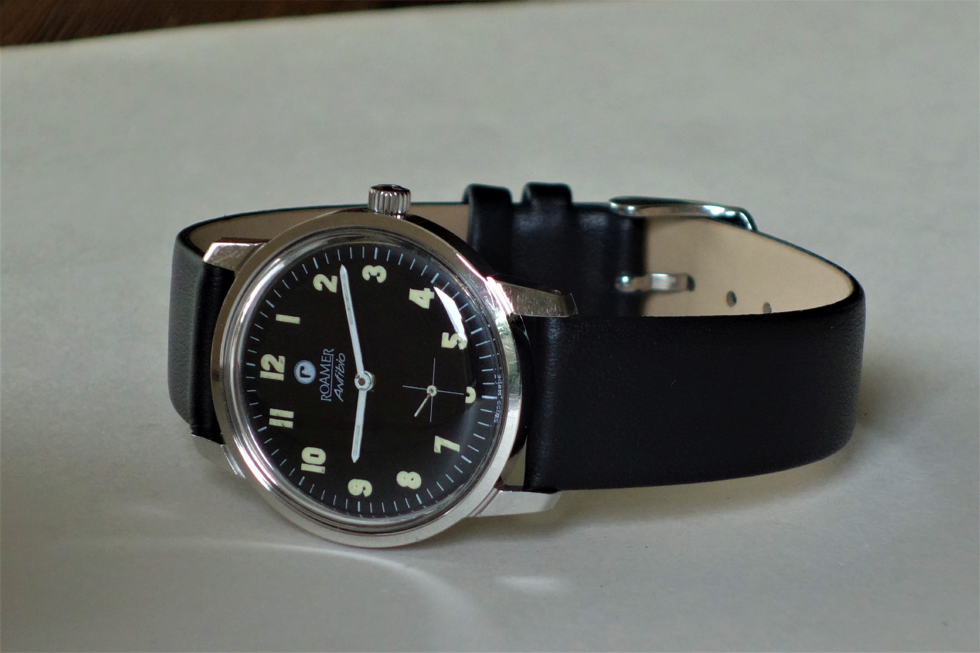 Schwarze Armbanduhr mit hellem Zifferblatt und schwarzem Armband.