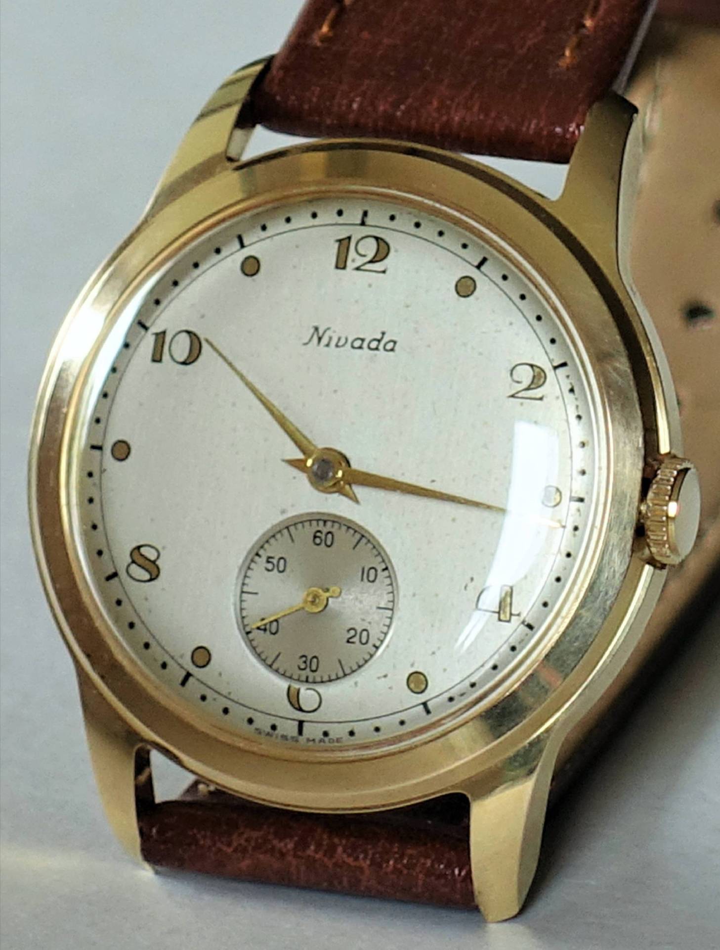 Goldfarbene Armbanduhr mit weißem Zifferblatt und braunem Lederarmband.