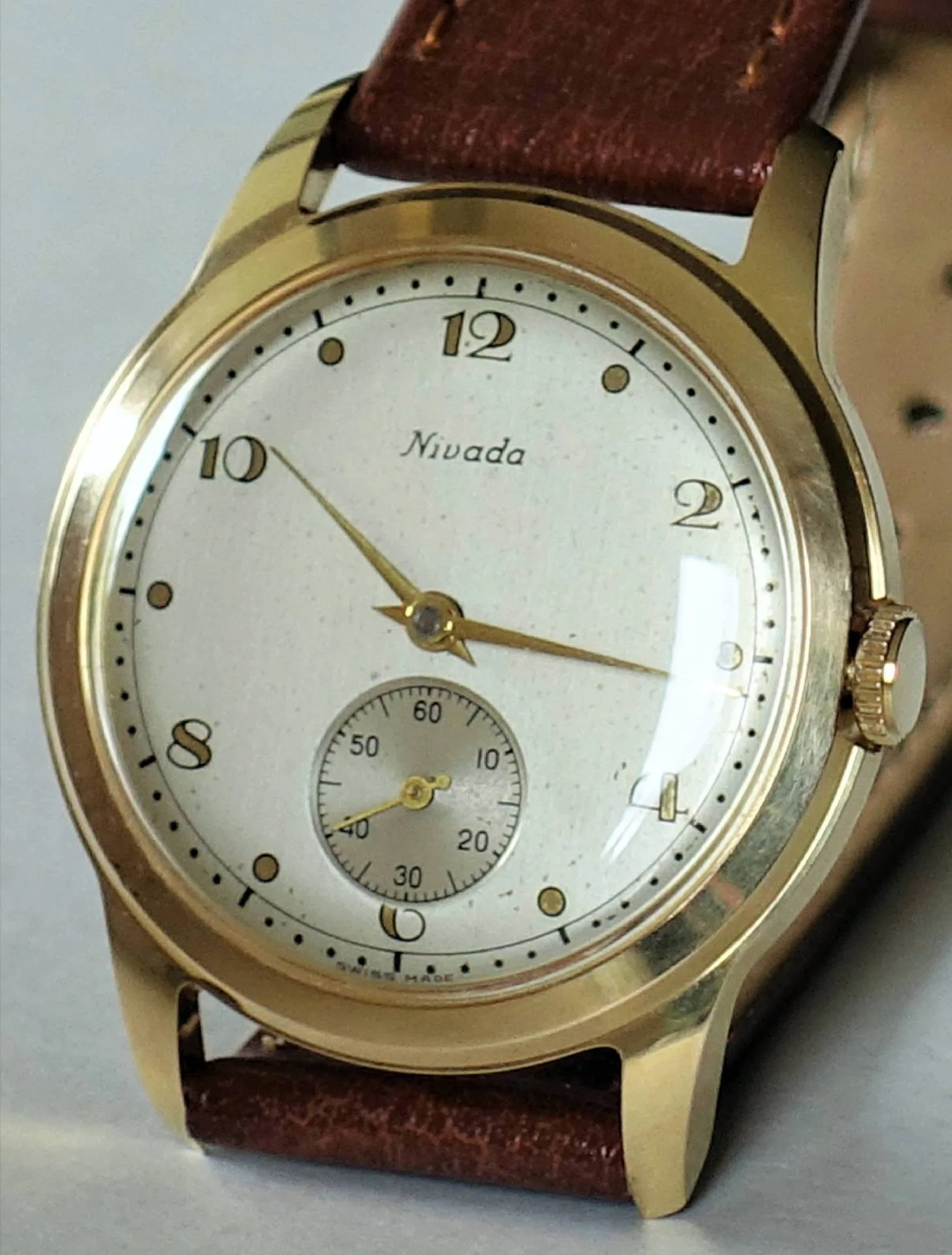Goldfarbene Armbanduhr mit weißem Zifferblatt und braunem Lederarmband.