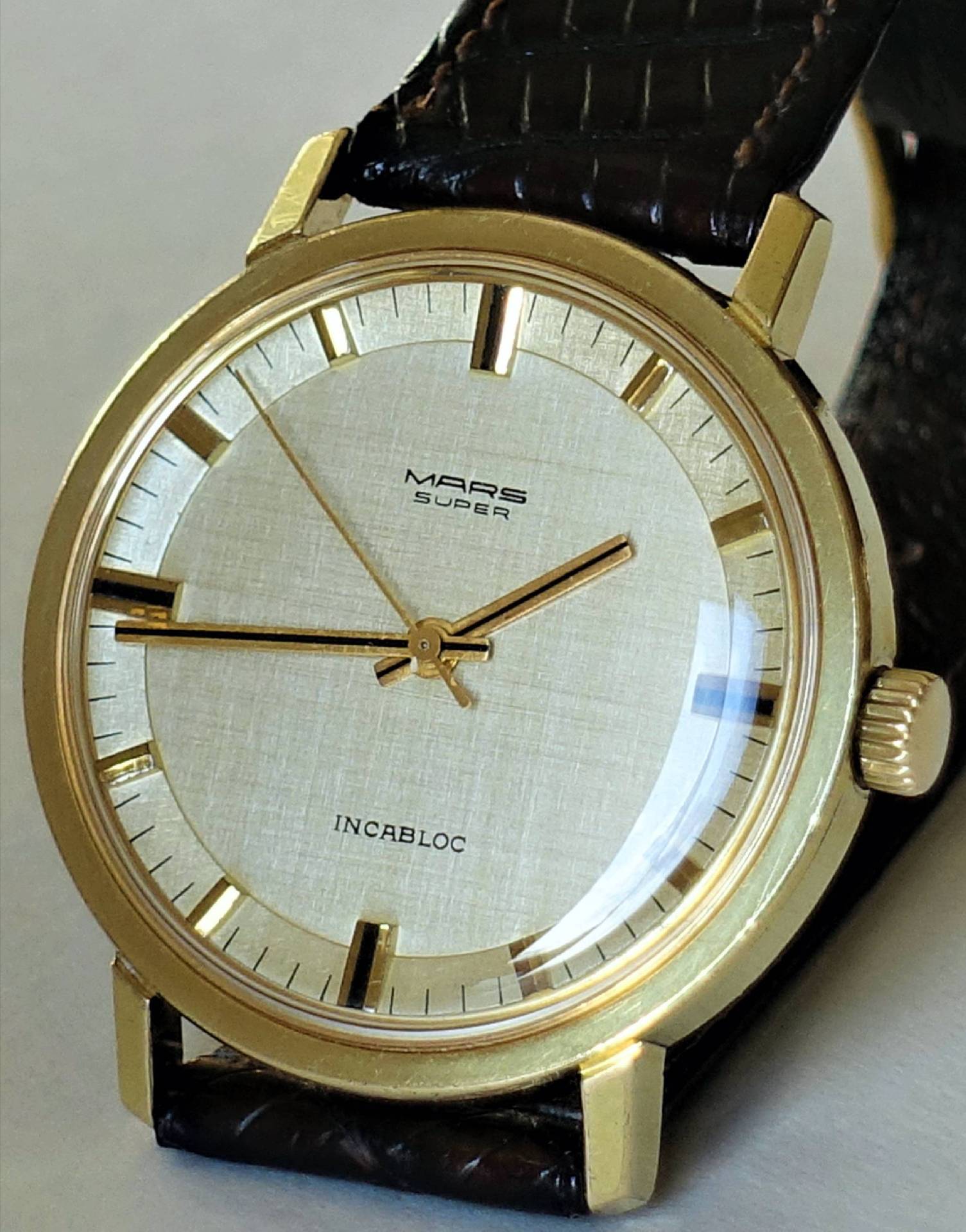 Goldfarbene Armbanduhr mit hellem Zifferblatt und braunem Armband.