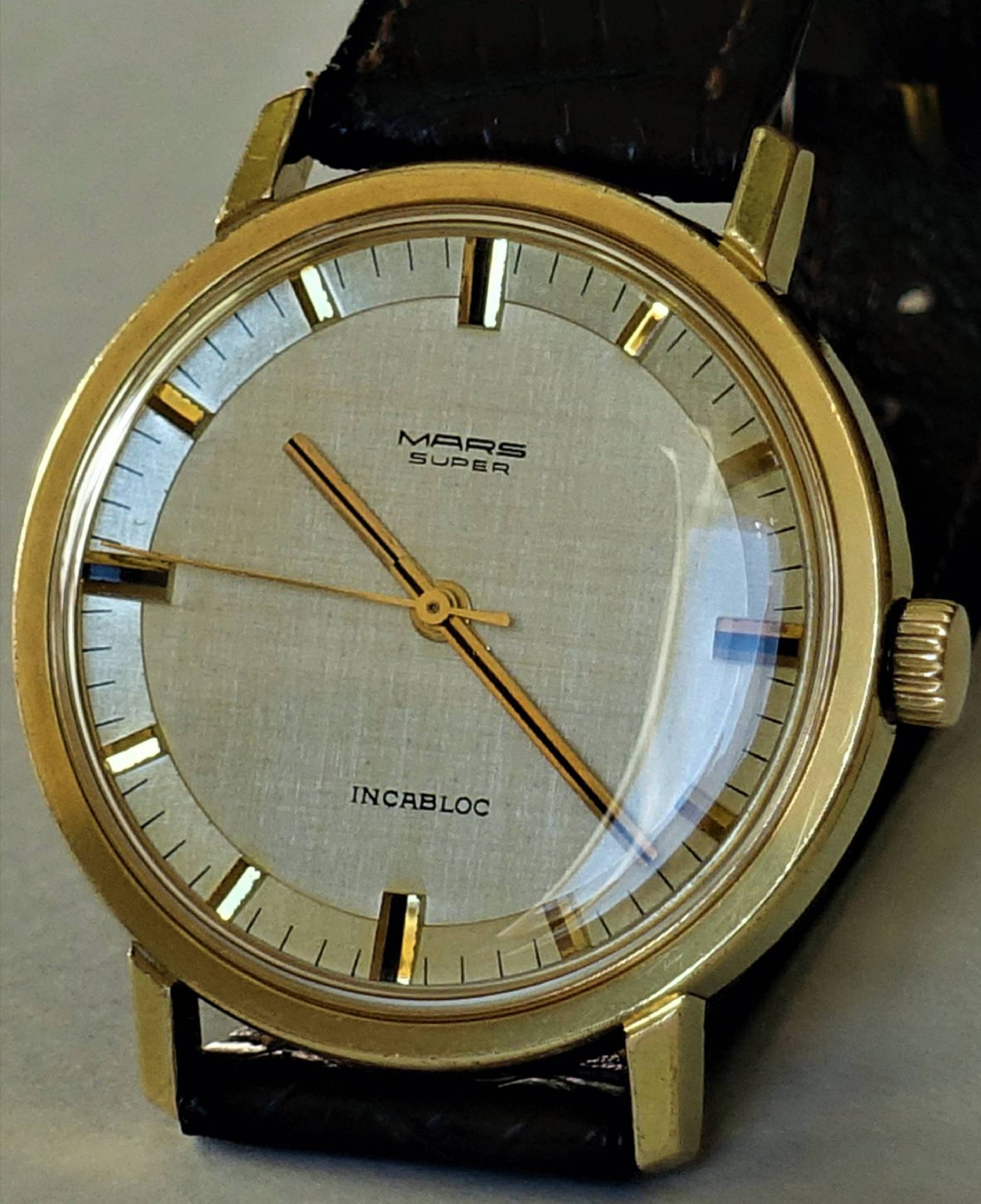 Goldfarbene analoge Armbanduhr mit hellem Zifferblatt und schwarzem Armband.