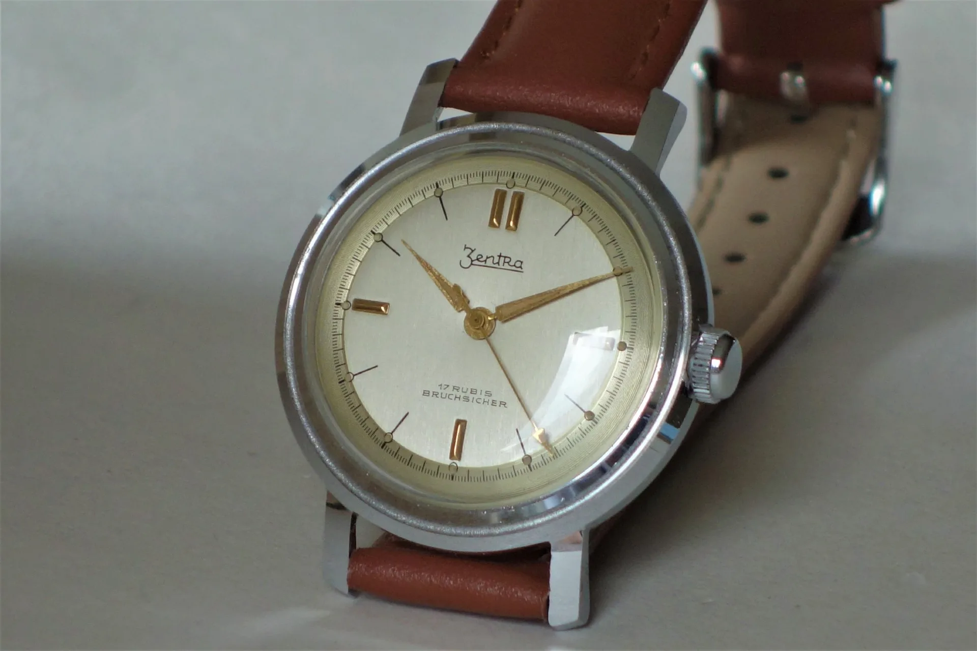 Mechanische Armbanduhr mit silberfarbenem Gehäuse, beigem Zifferblatt und braunem Armband.