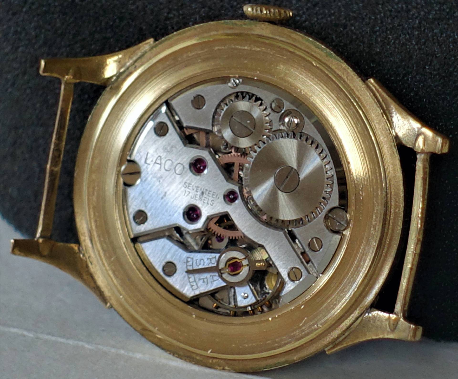 Silberfarbenes mechanisches Uhrwerk in einem goldfarbenen Uhrengehäuse, sichtbare Zahnräder und Schrauben.