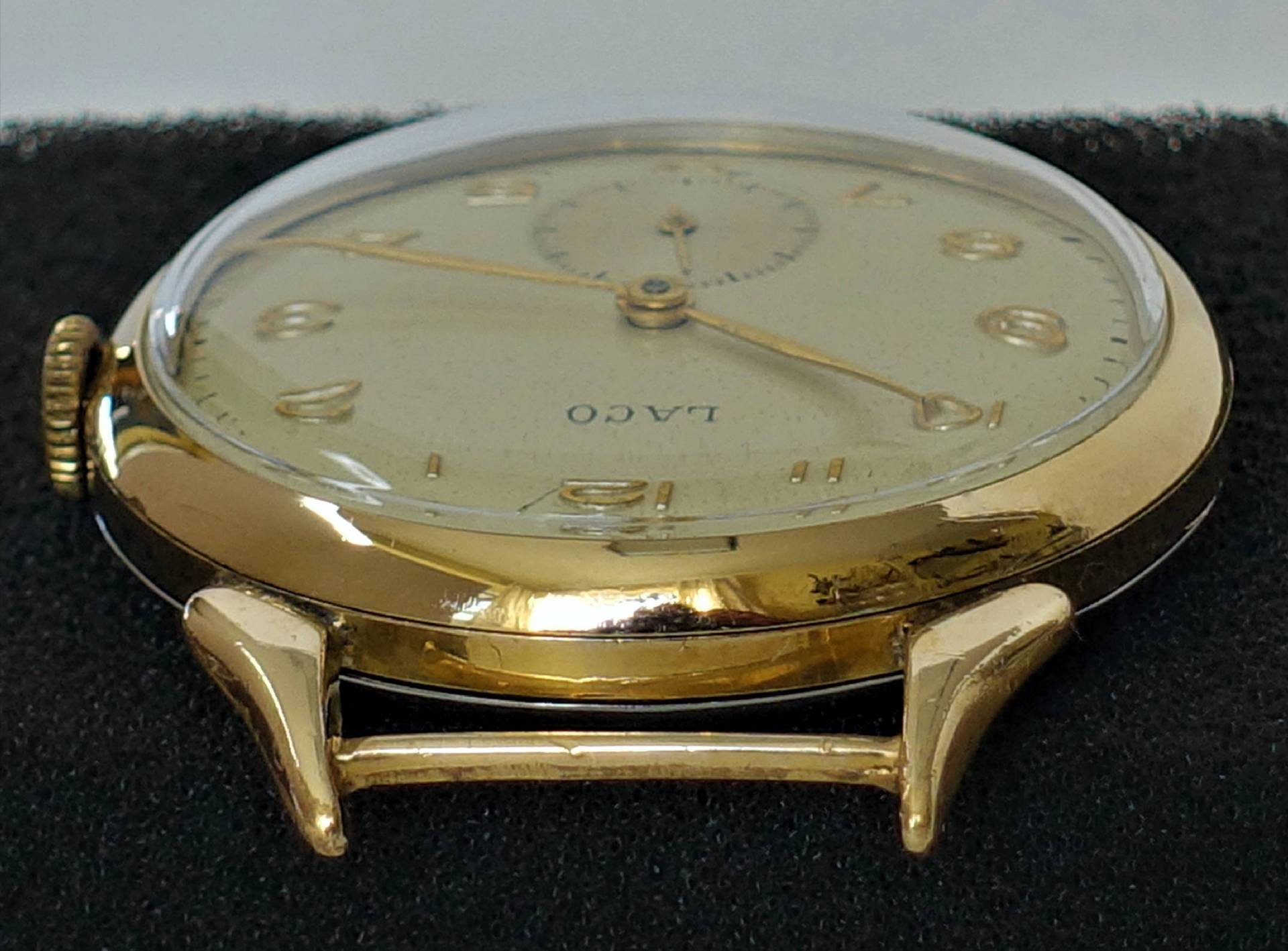 Flache Armbanduhr mit goldfarbenem Gehäuse und hellem Zifferblatt, Aufschrift "LACO".