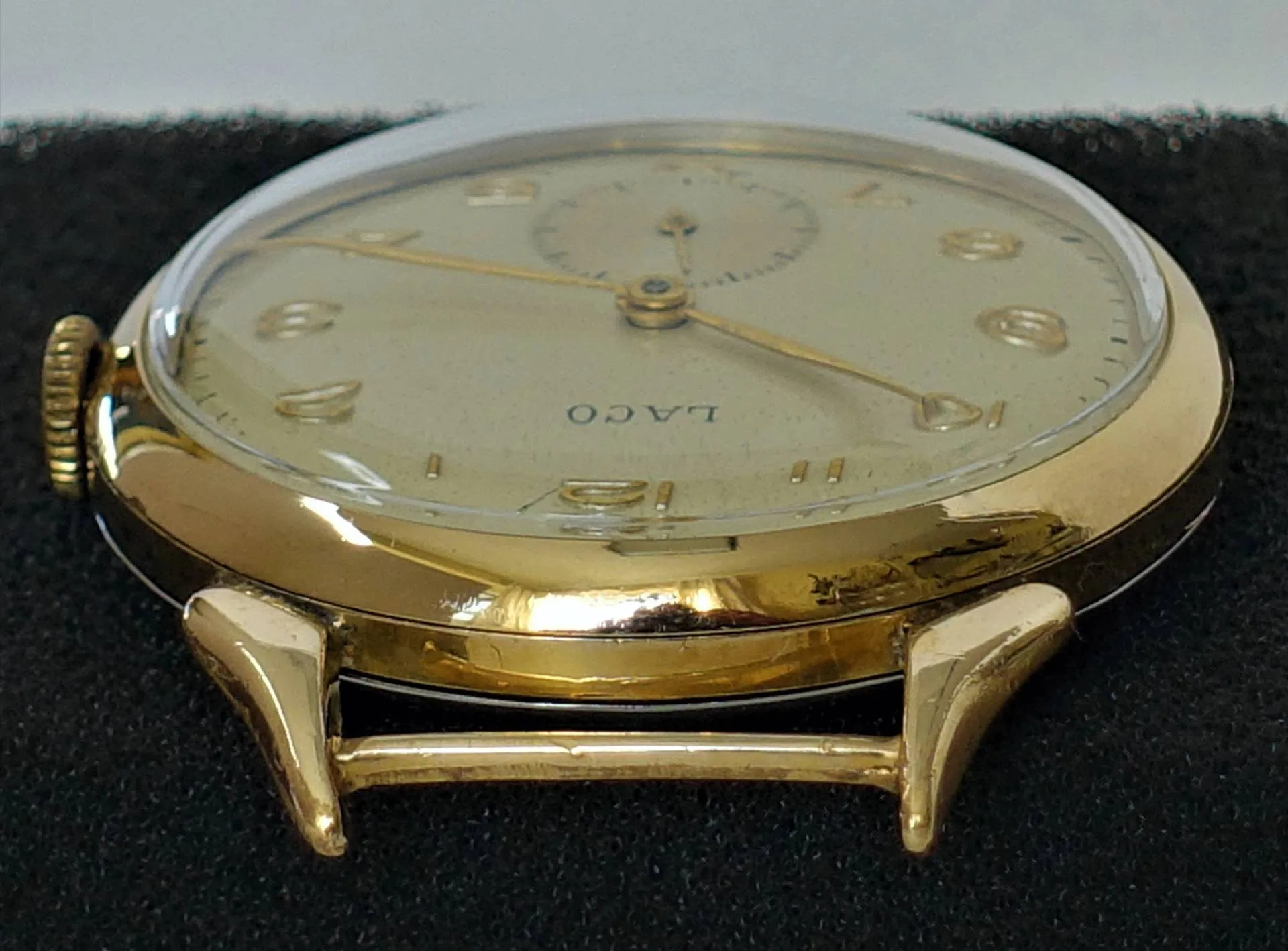 Flache Armbanduhr mit goldfarbenem Gehäuse und hellem Zifferblatt, Aufschrift "LACO".