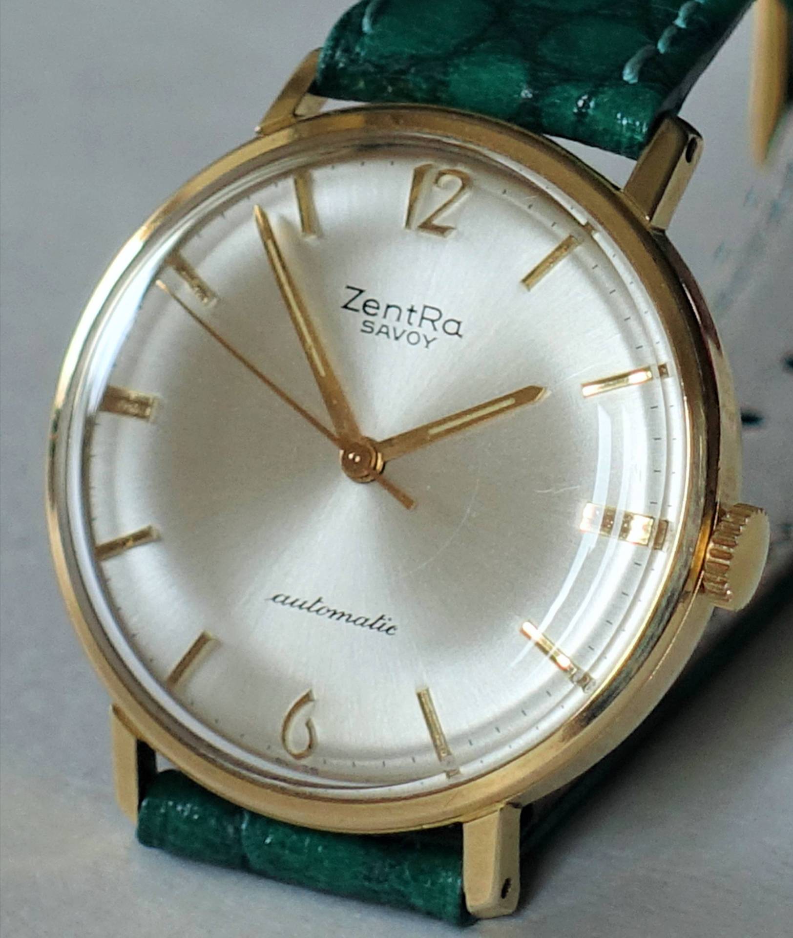 Goldfarbene Armbanduhr mit hellem Zifferblatt und grünem Armband.