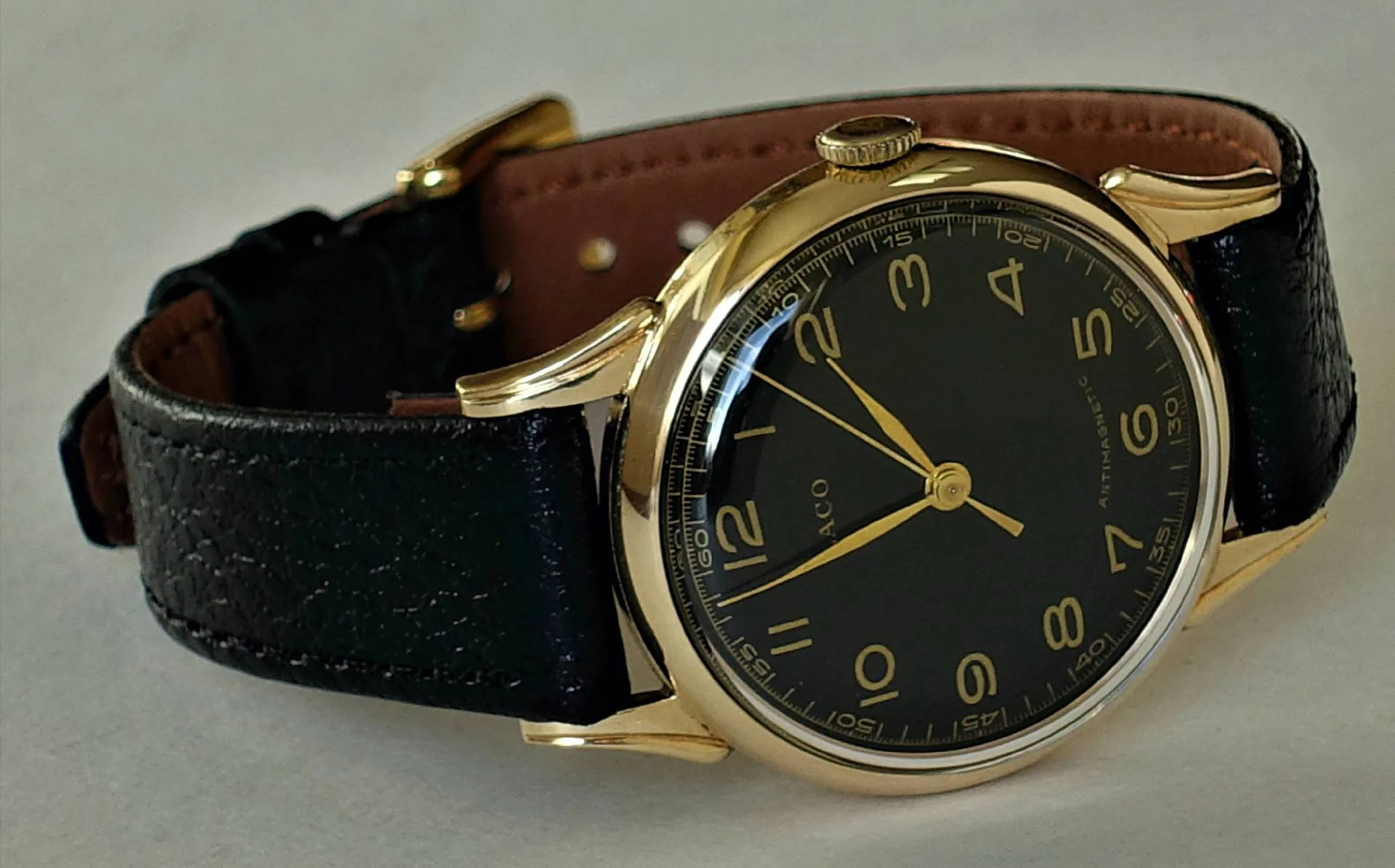 Schwarzes Zifferblatt, gelbfarbenes Gehäuse Eine Armbanduhr mit schwarzem Zifferblatt, gelbfarbenem Gehäuse und schwarzem Lederarmband liegt auf einer hellen Oberfläche.
