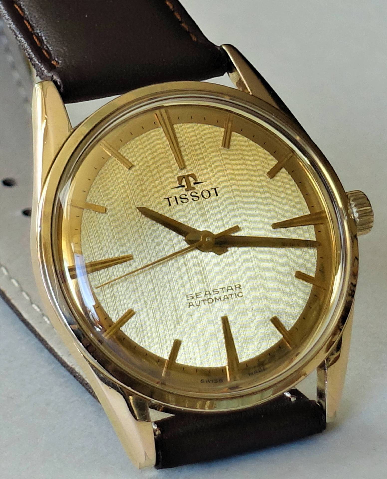 Goldfarbene Armbanduhr mit braunem Armband und hellem Zifferblatt, Modell Tissot Seastar Automatic.