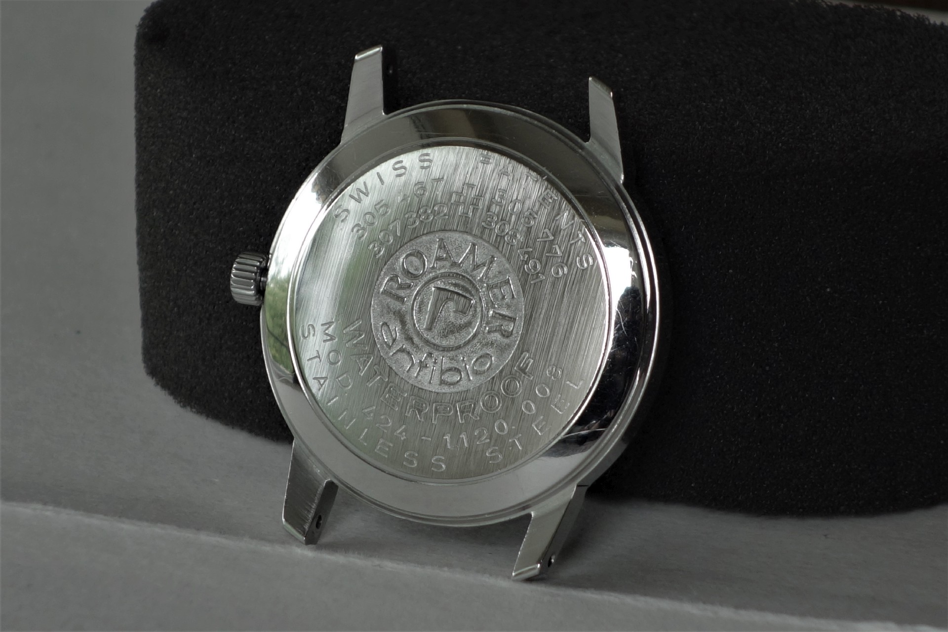 Silberfarbenes Uhrengehäuse mit graviertem Boden und seitlicher Krone.