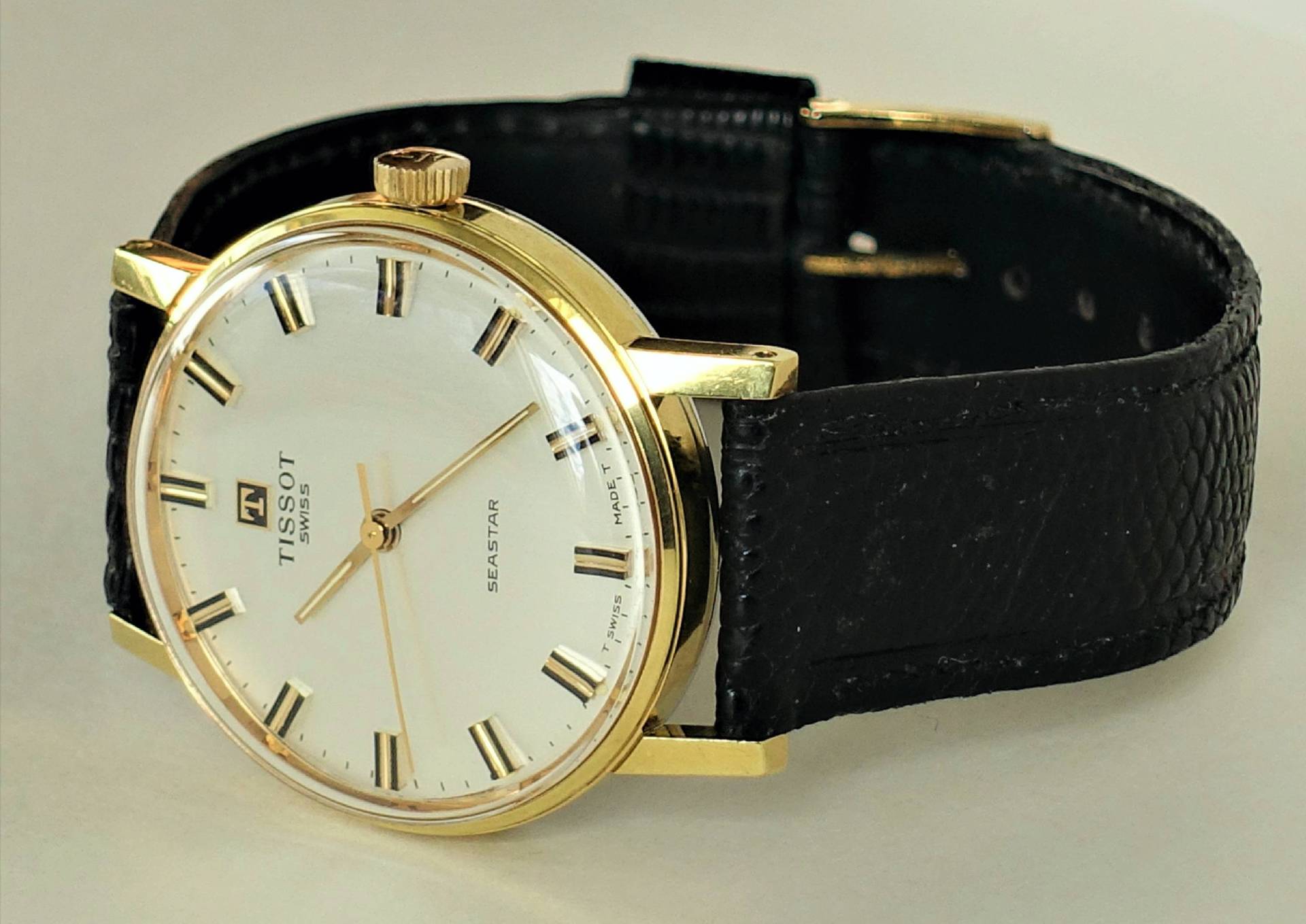 Klassische Armbanduhr mit goldfarbenem Gehäuse, weißem Zifferblatt und schwarzem Armband.