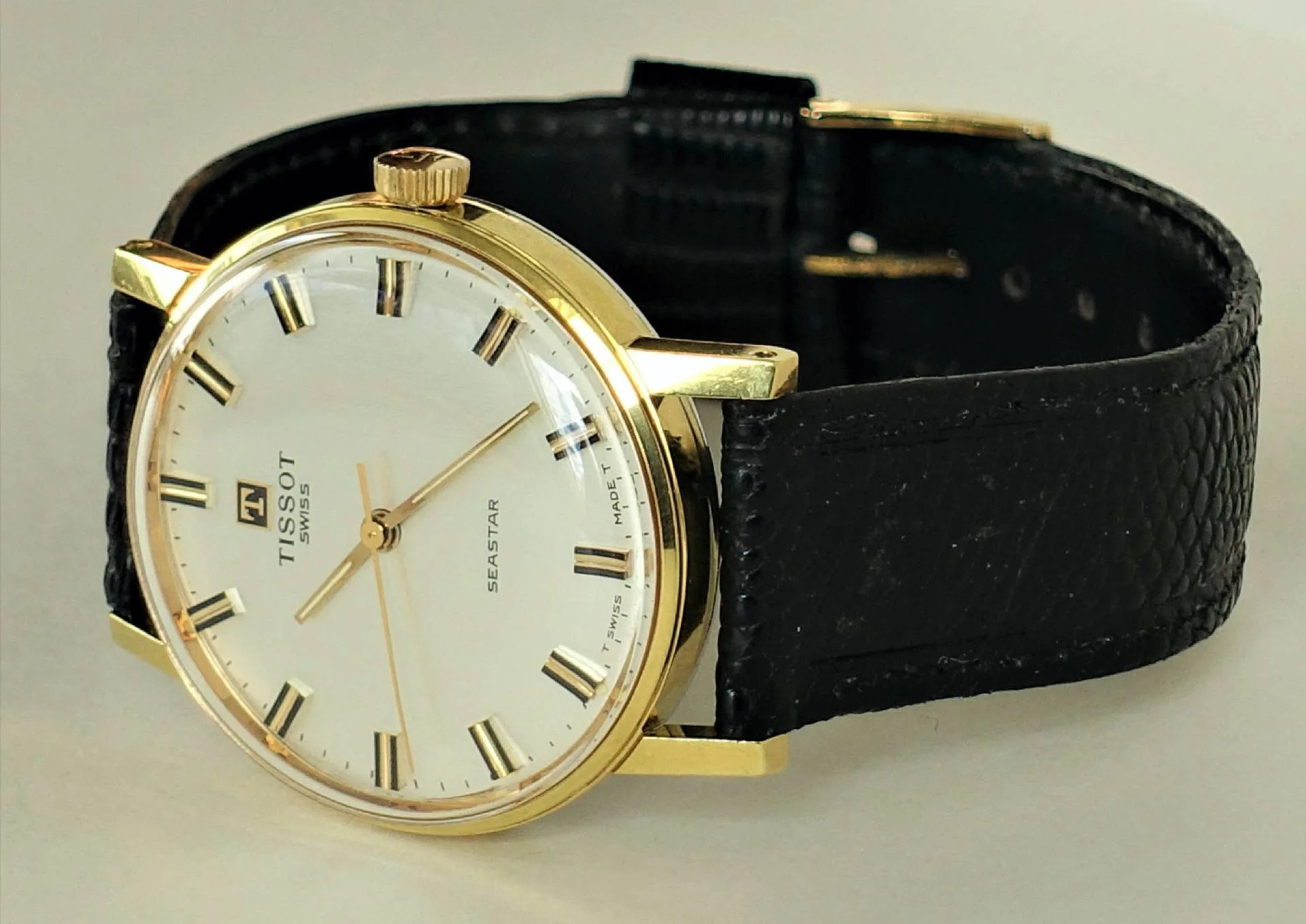 Klassische Armbanduhr mit goldfarbenem Gehäuse, weißem Zifferblatt und schwarzem Armband.