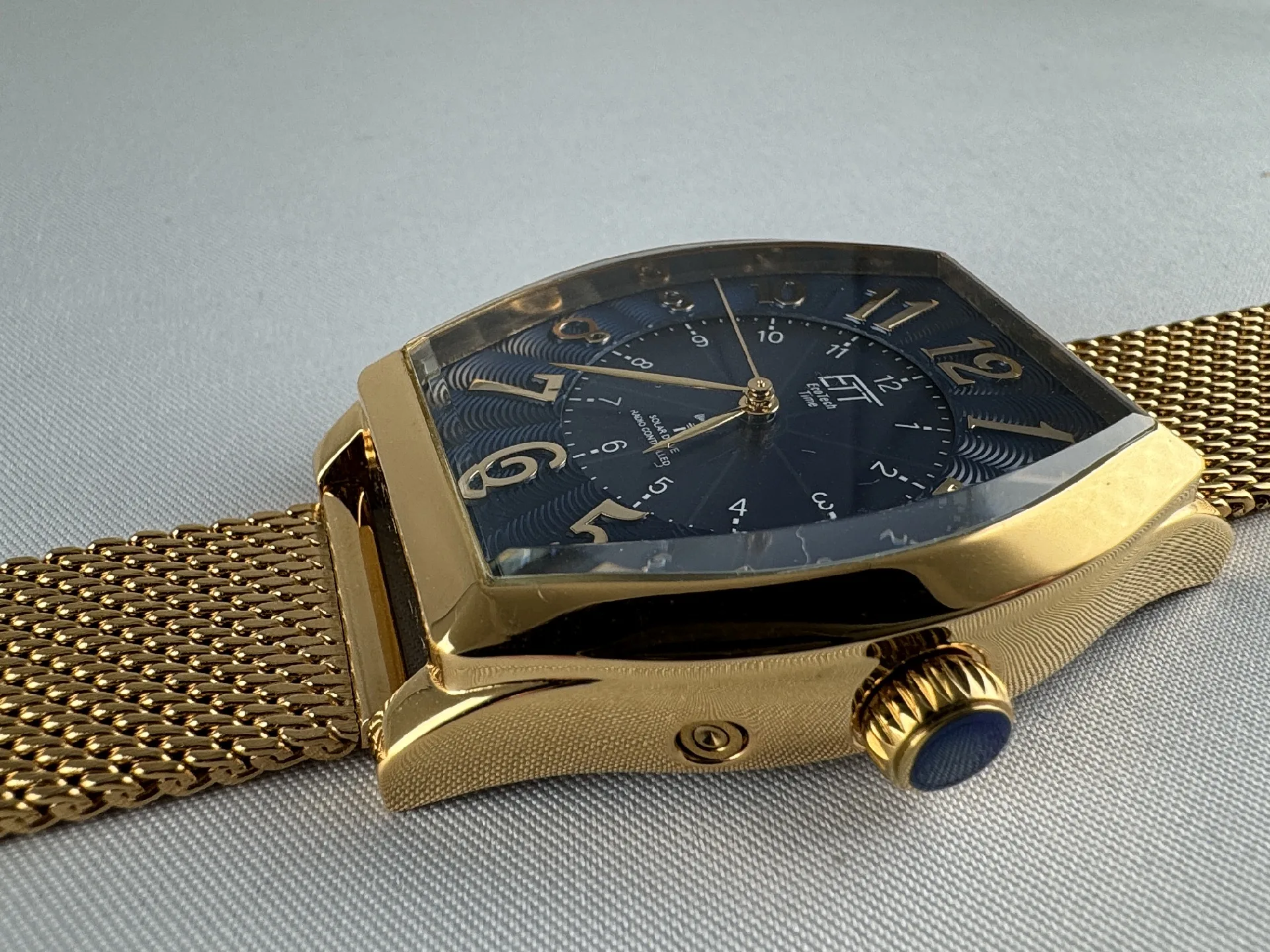 Goldfarbene Armbanduhr mit eckigem Gehäuse, blauem Zifferblatt und goldfarbenem Milanaise-Edelstahlarmband.