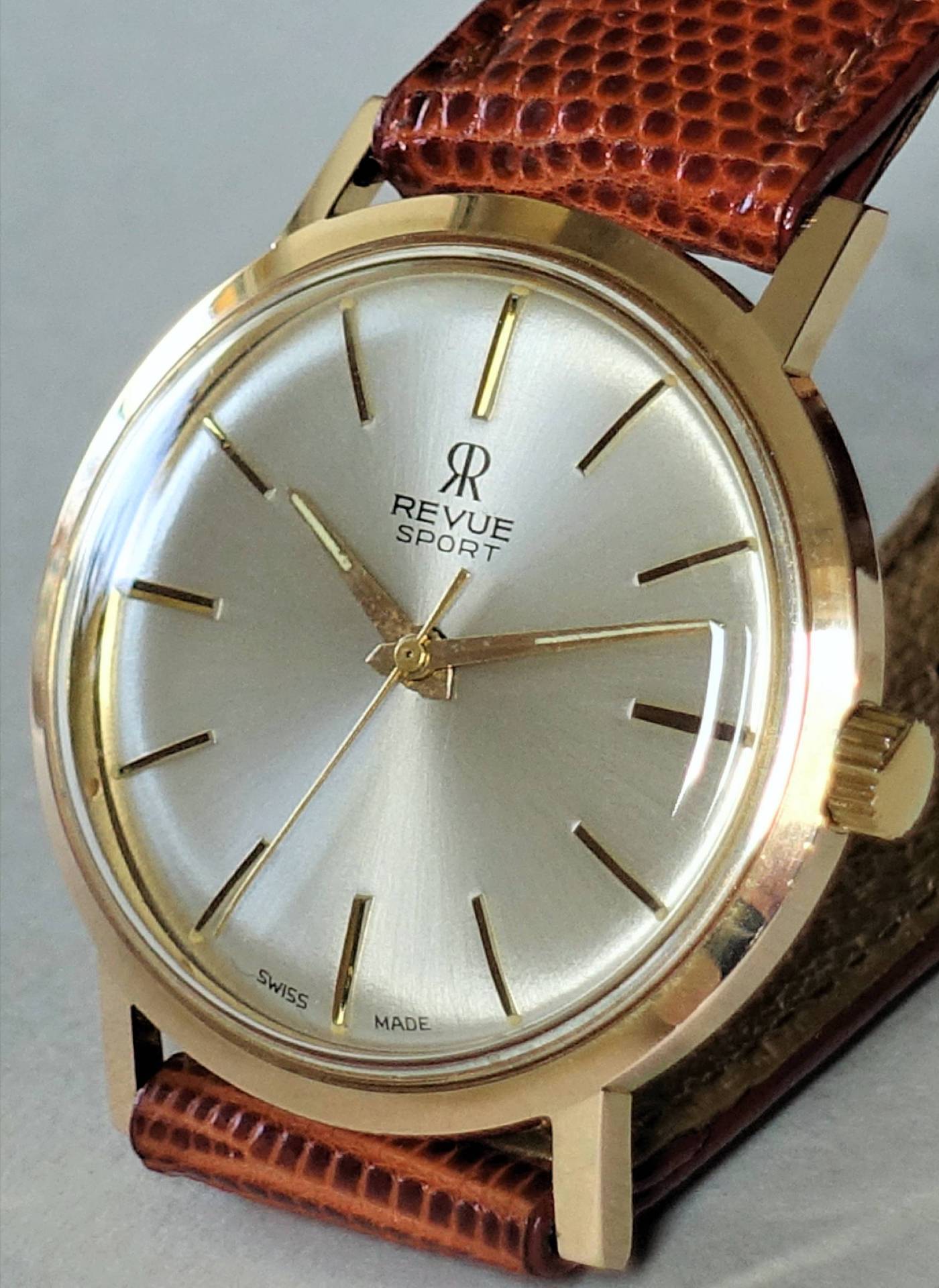 Goldfarbene Armbanduhr mit silberfarbenem Zifferblatt und braunem Armband.