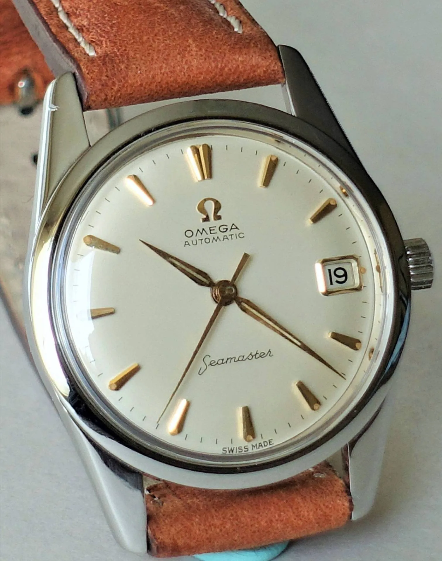 Omega Seamaster Armbanduhr Silberfarbene Armbanduhr mit beigem Zifferblatt, goldfarbenen Indizes und braunem Lederarmband.