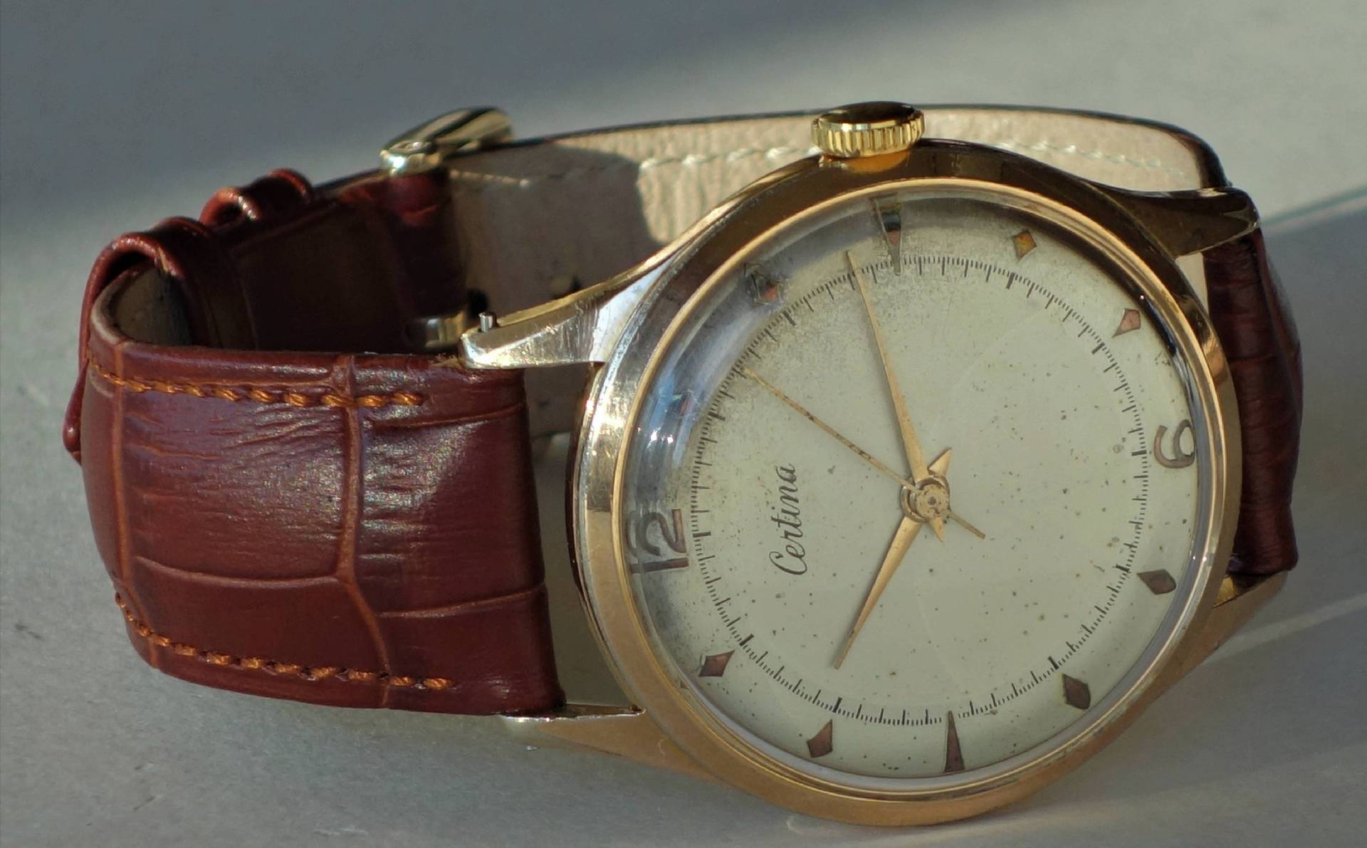 Analoge Armbanduhr mit braunem Armband und goldfarbenem Gehäuse.