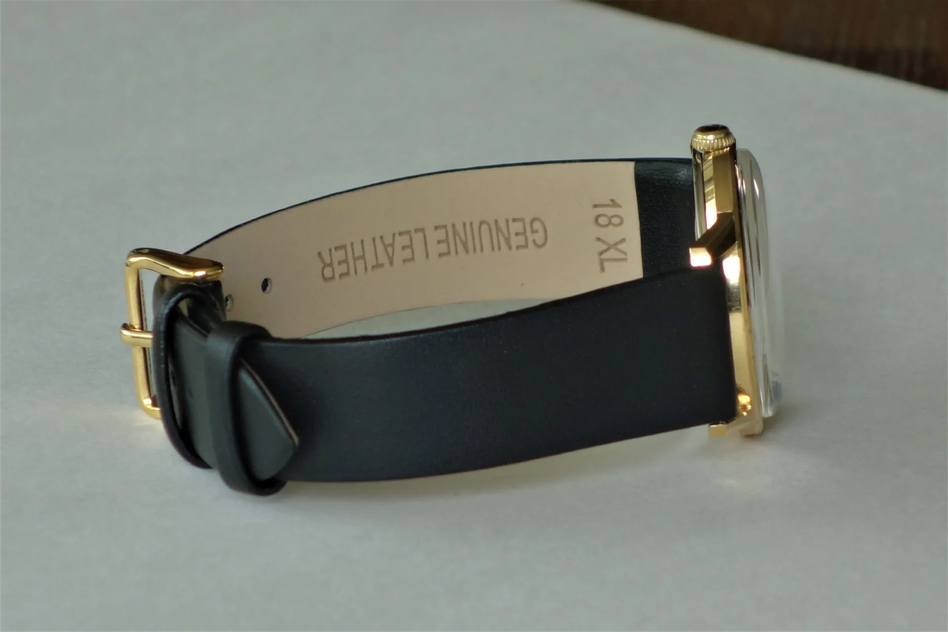 Schwarzes Lederarmband mit goldfarbener Schließe an einer Uhr.