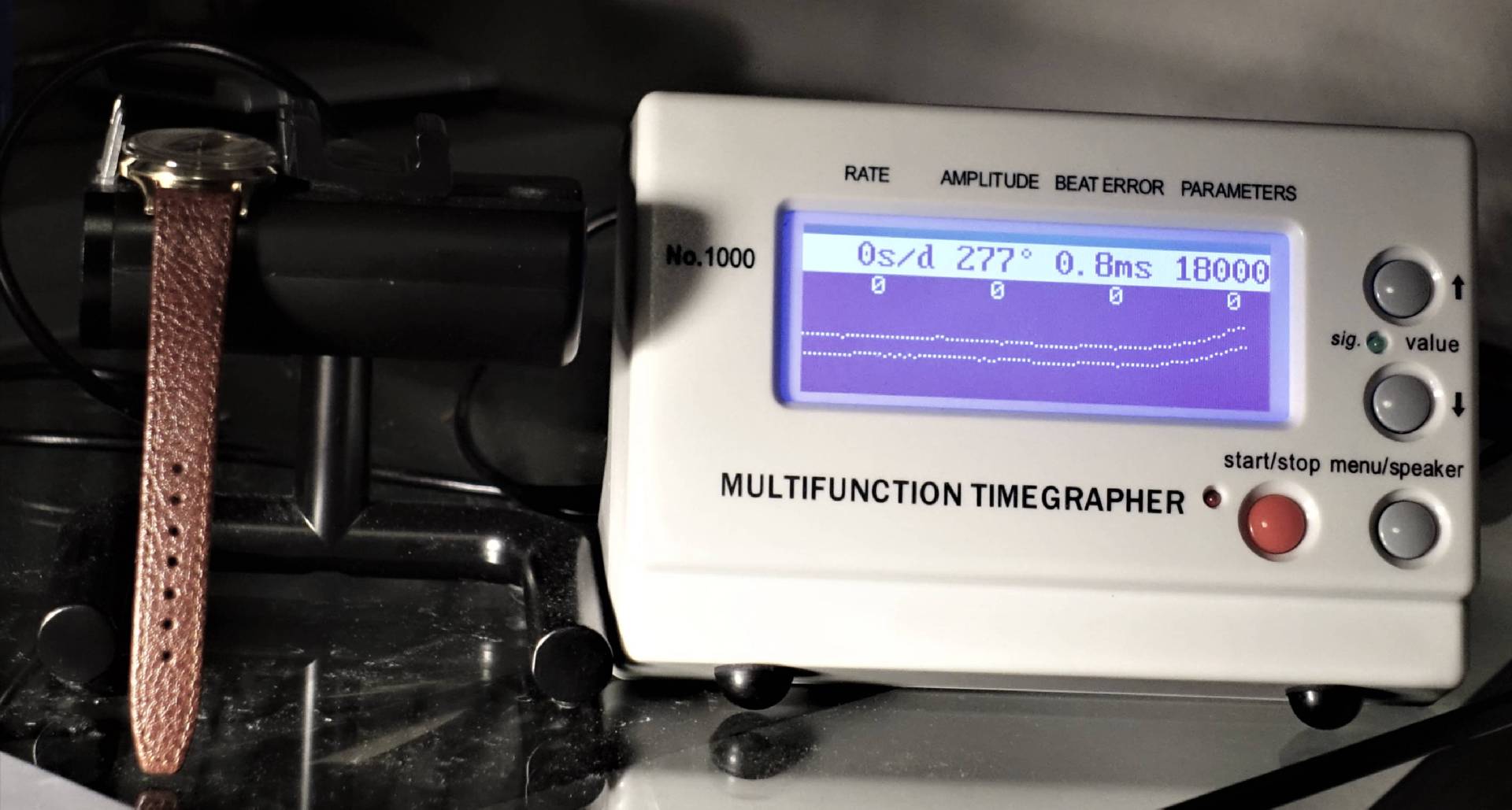 Weißes elektronisches Messgerät zur Überprüfung von mechanischen Uhren mit digitaler Anzeige.
