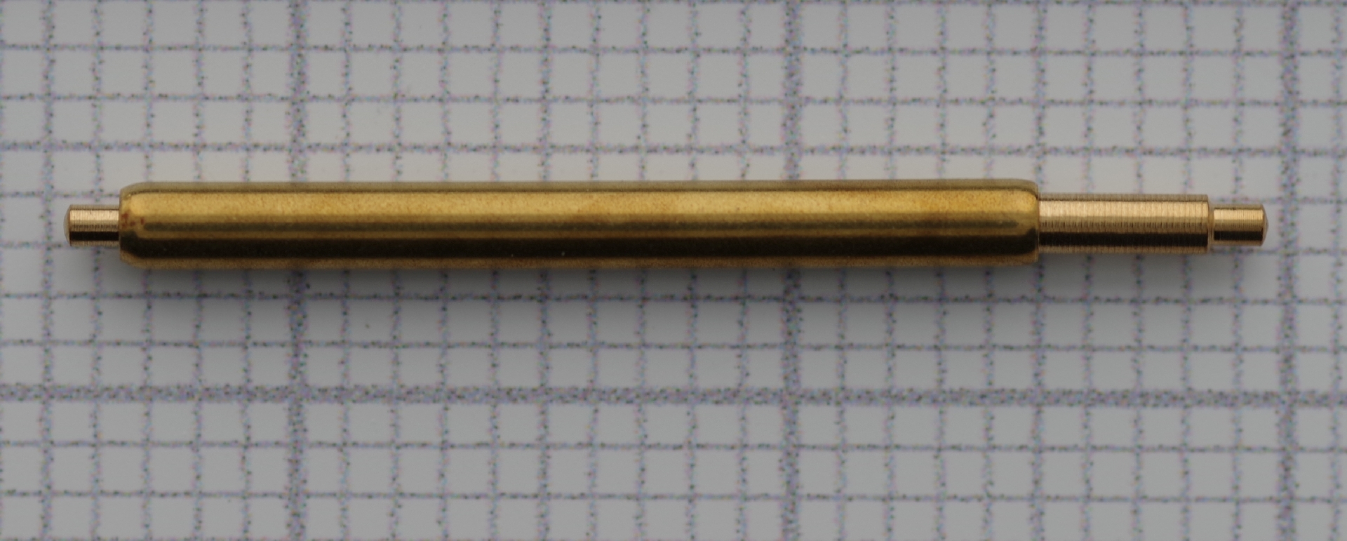 Zylindrische Aufzugswelle aus Messing für Uhrwerke, auf kariertem Hintergrund.