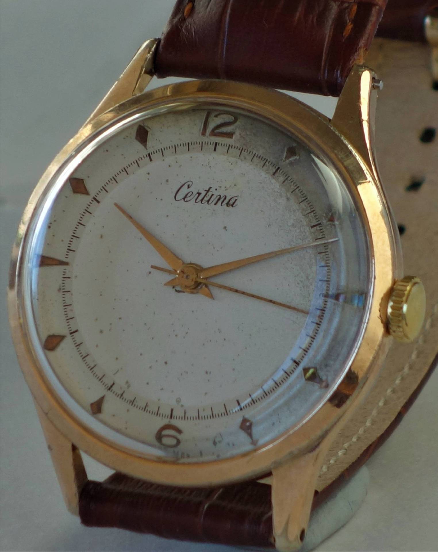 Analoge Armbanduhr mit goldfarbenem Gehäuse, weißem Zifferblatt und braunem Armband.