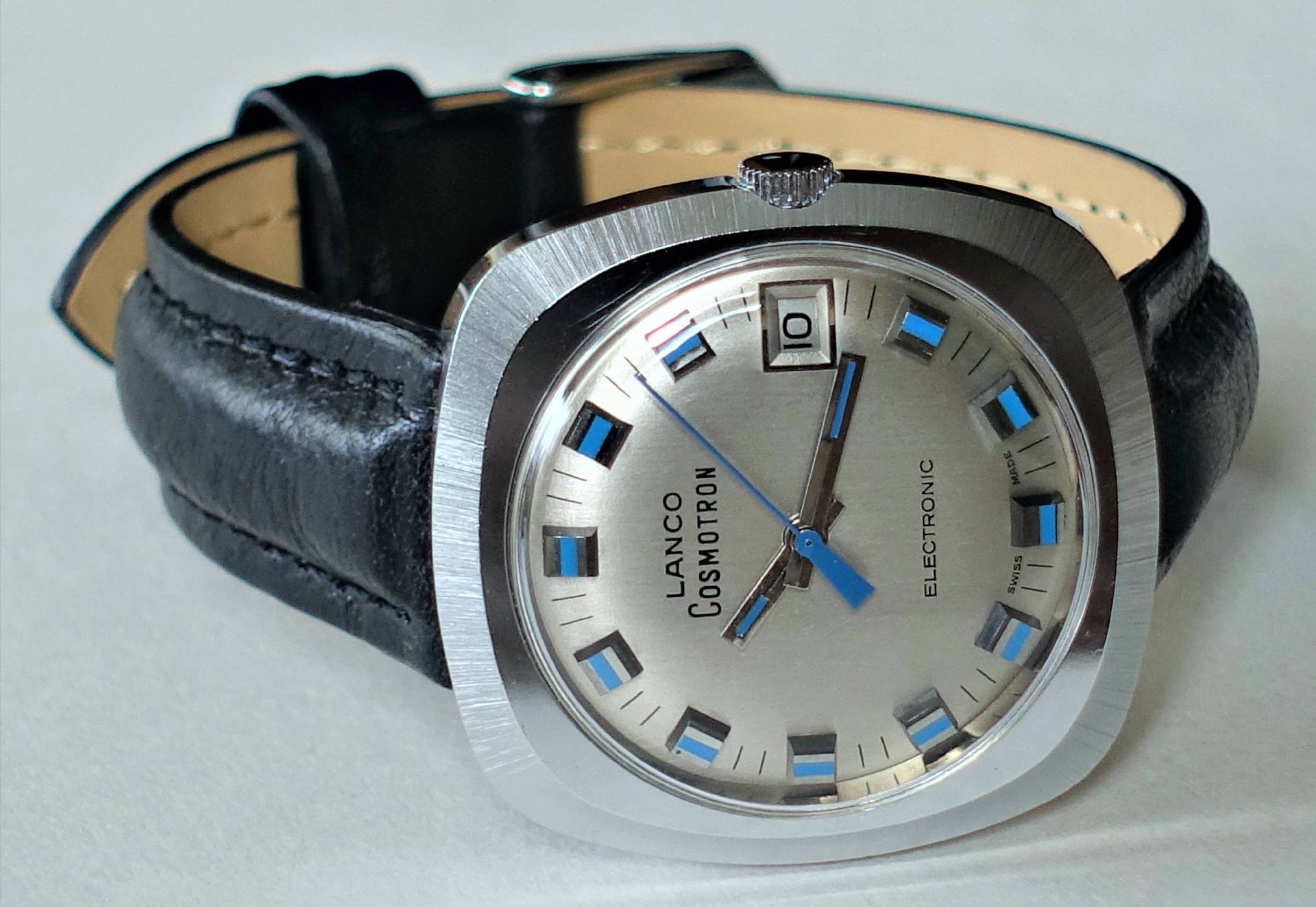 Silberfarbene Armbanduhr mit schwarzem Lederarmband und blau-silbernem Zifferblatt, Datumsanzeige bei drei Uhr.