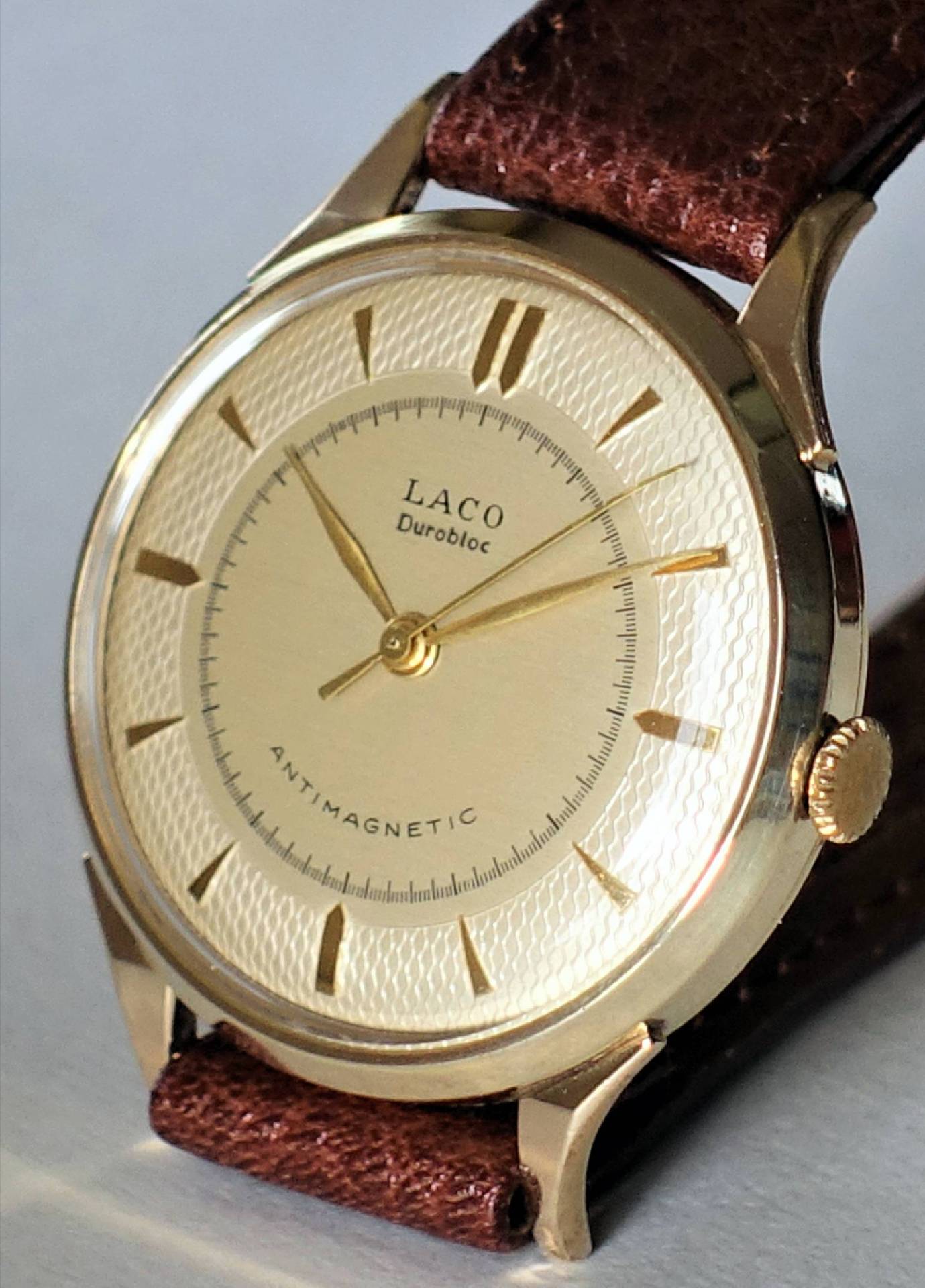 Goldfarbene Armbanduhr mit braunem Armband und hellem Zifferblatt.