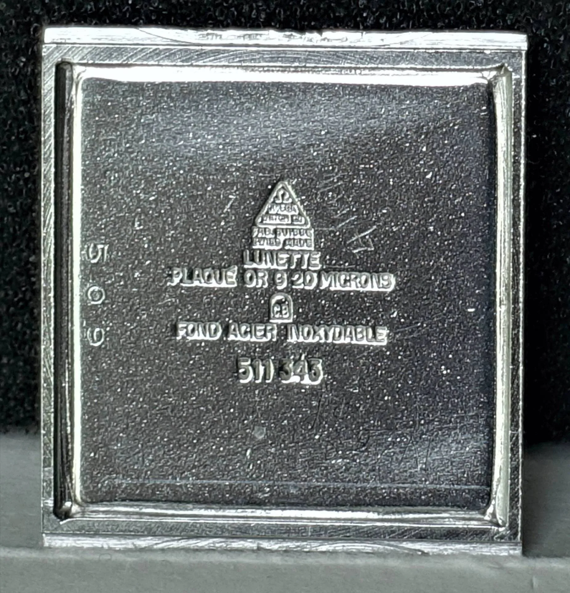 Quadratischer silberfarbener Gehäuseboden für Armbanduhren mit Prägung und Gravur.