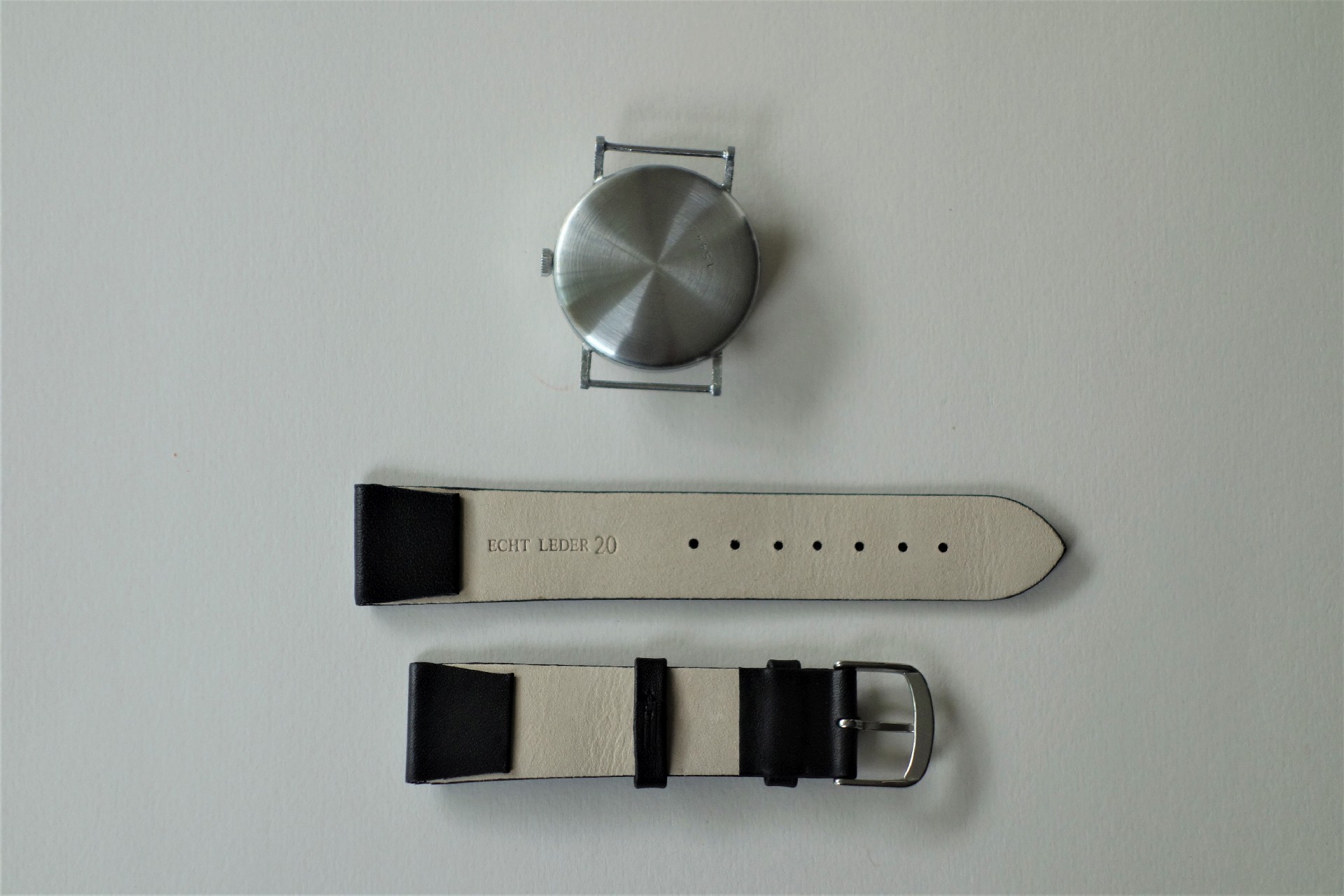 Silberfarbenes rundes Uhrgehäuse mit schwarzem Lederarmband in zwei Teilen.