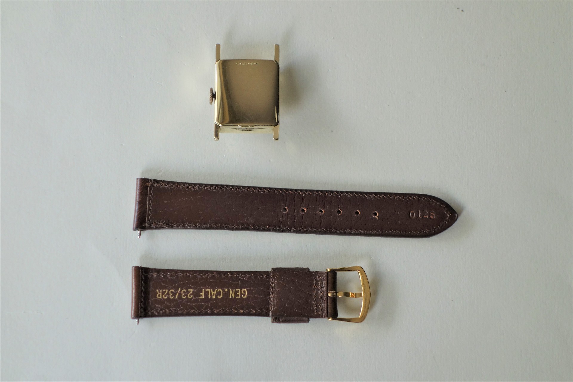 Rechteckiges Uhrengehäuse in Goldfarbe mit braunem Lederarmband in zwei Teilen und goldfarbener Schließe.
