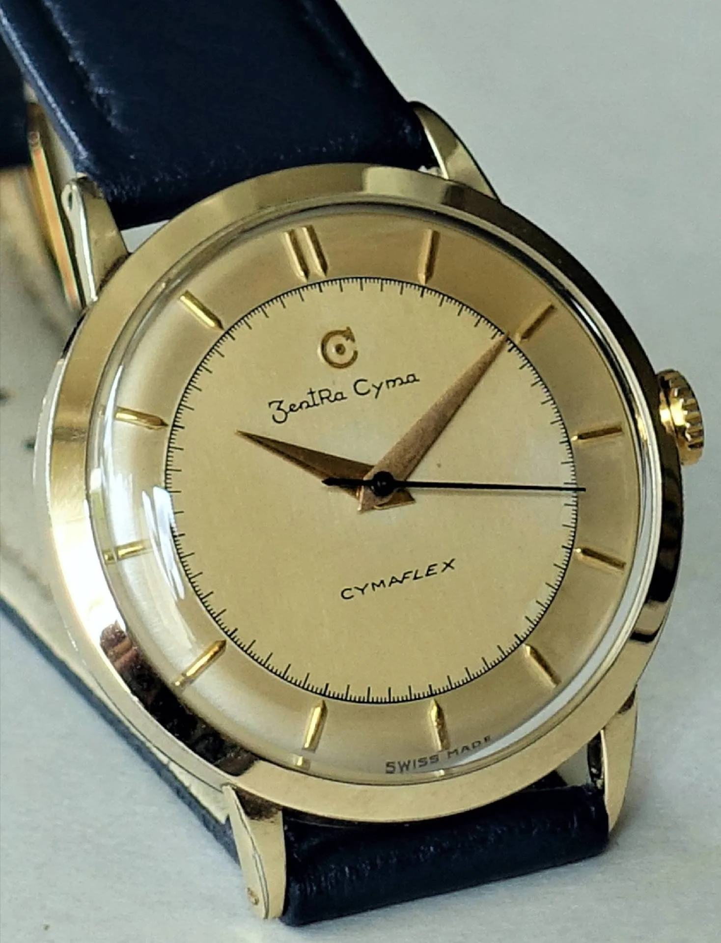 ZentRa Cyma Armbanduhr Goldfarbene Armbanduhr mit hellem Zifferblatt und schwarzem Lederarmband.