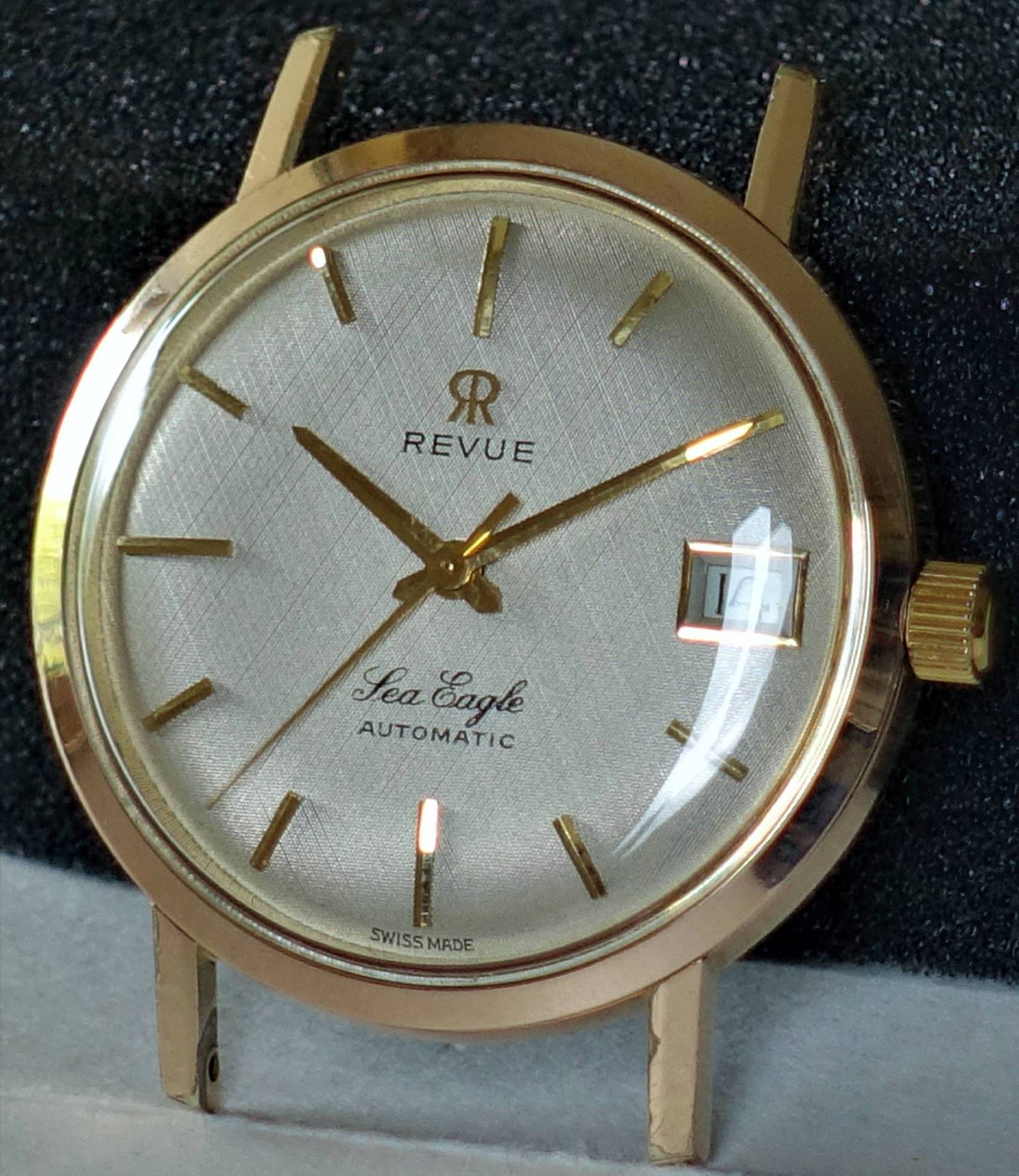 Goldfarbene Armbanduhr mit silberfarbenem Zifferblatt, goldenen Zeigern und Datumsanzeige.
