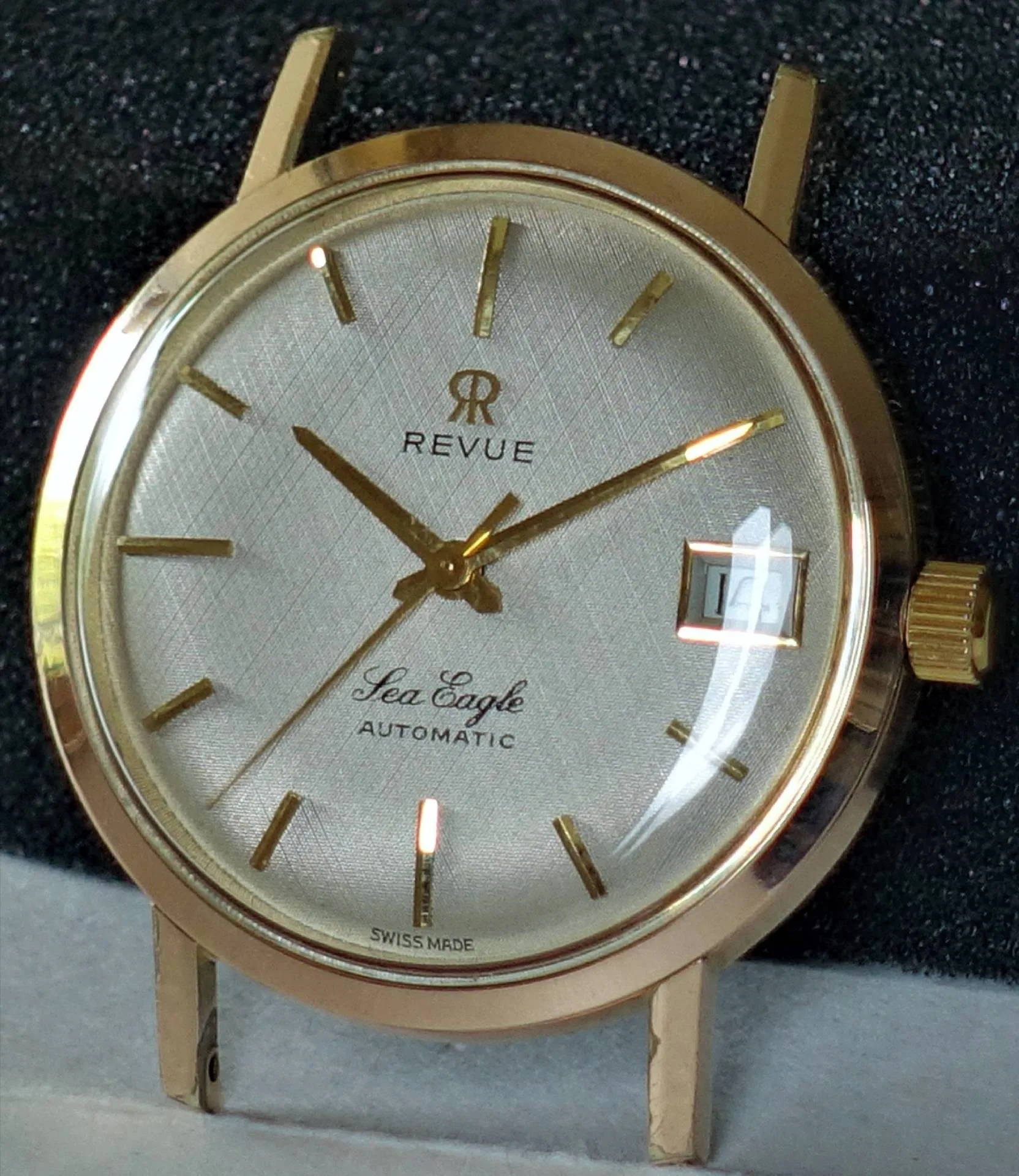Goldfarbene Armbanduhr mit silberfarbenem Zifferblatt, goldenen Zeigern und Datumsanzeige.