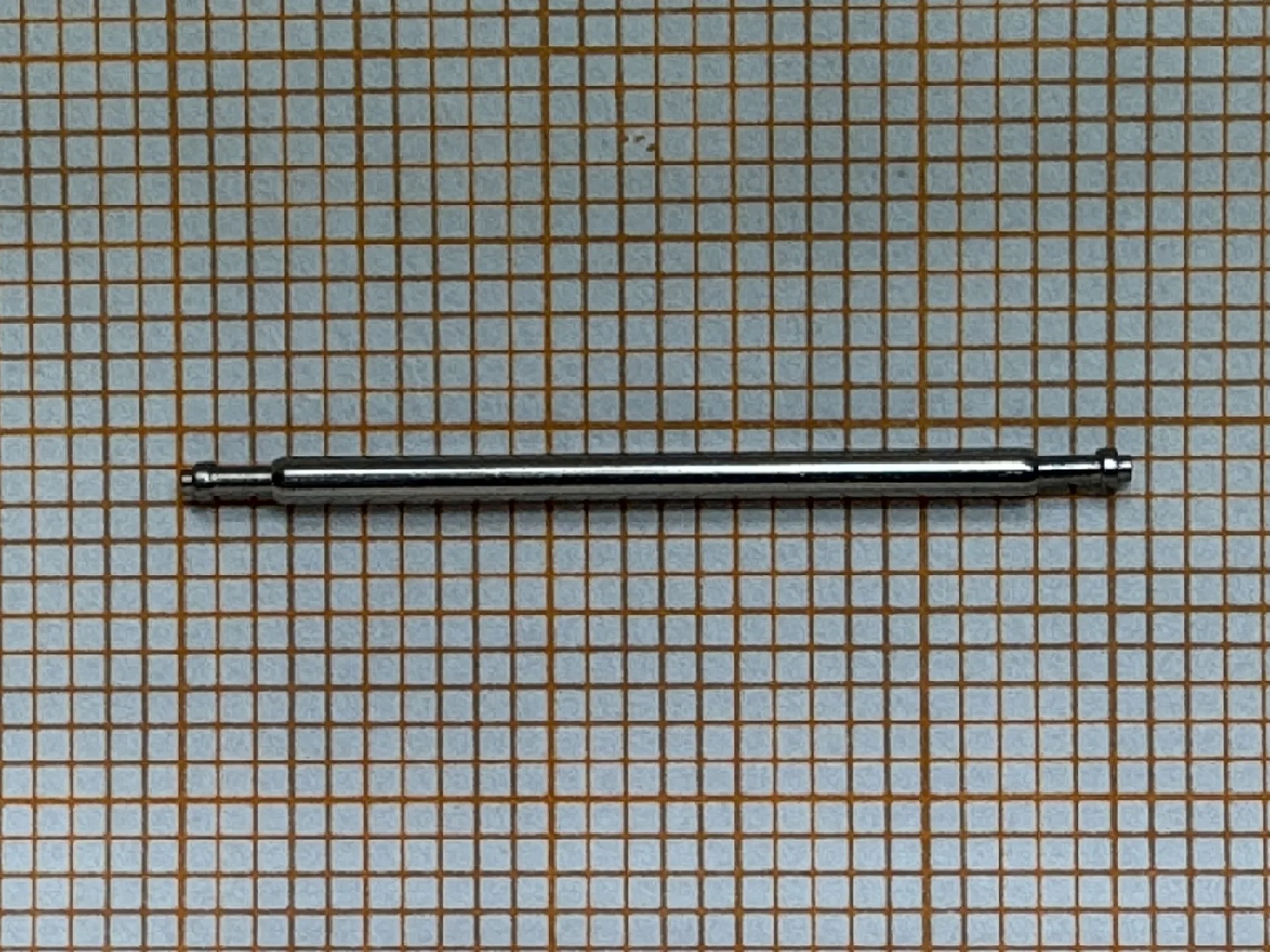 Federsteg Metall Metallischer Federsteg für Uhrenarmbänder auf kariertem Hintergrund.