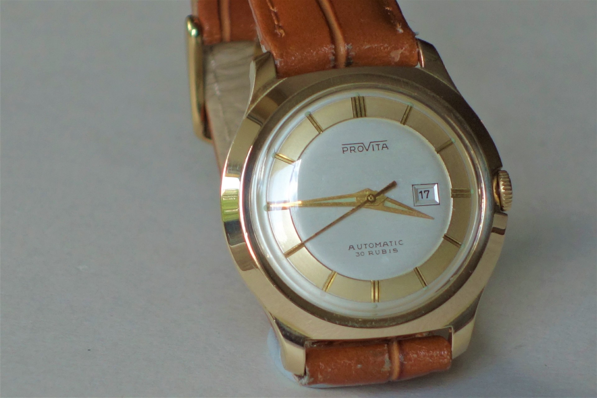 Analoge Armbanduhr mit braunem Band und hellem Zifferblatt.