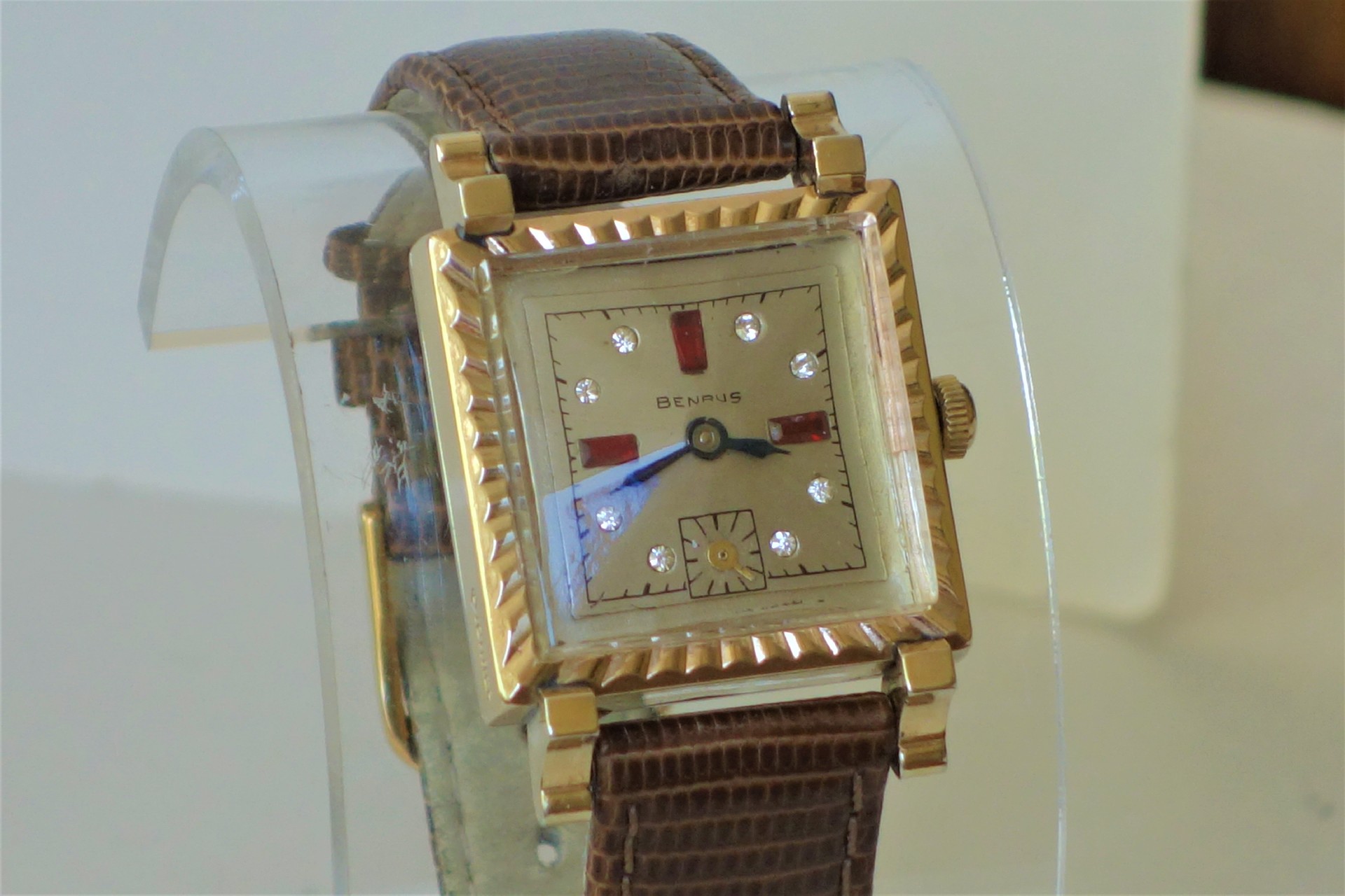 Eckige Armbanduhr der Marke Benrus mit goldfarbenem Gehäuse, Zifferblatt mit Schmucksteinen und braunem Lederarmband.